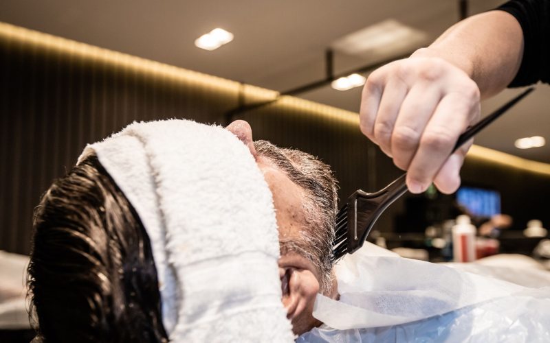 Homme au fauteuil pendant la pose d'une coloration au pinceau chez le coiffeur