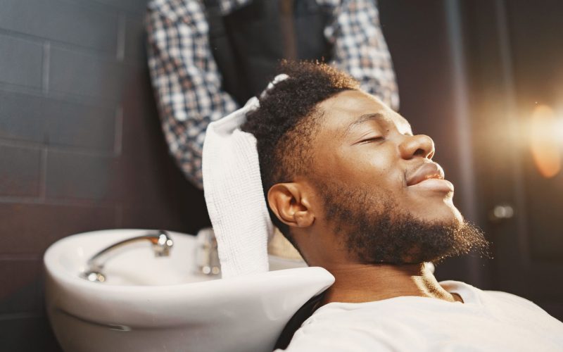Homme souriant au bac à shampoing, une serviette sur les épaules
