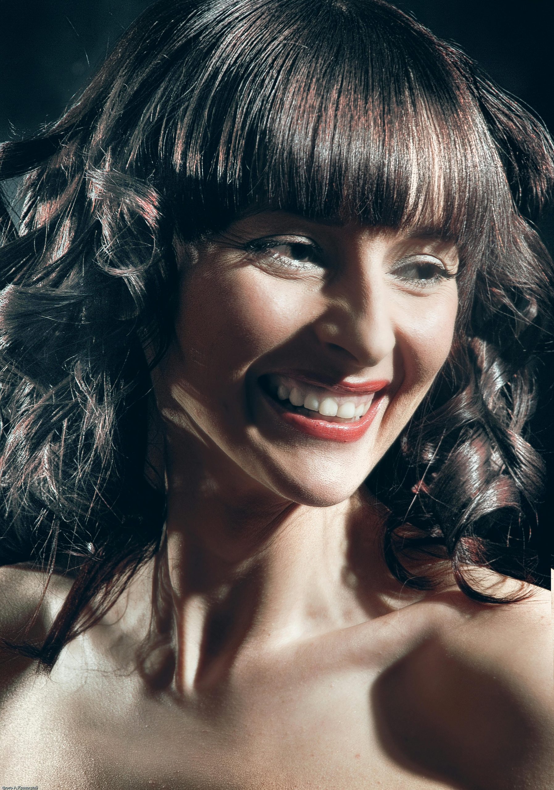 Portrait d'une femme joyeuse aux cheveux bouclés et frange, souriant avec éclat
