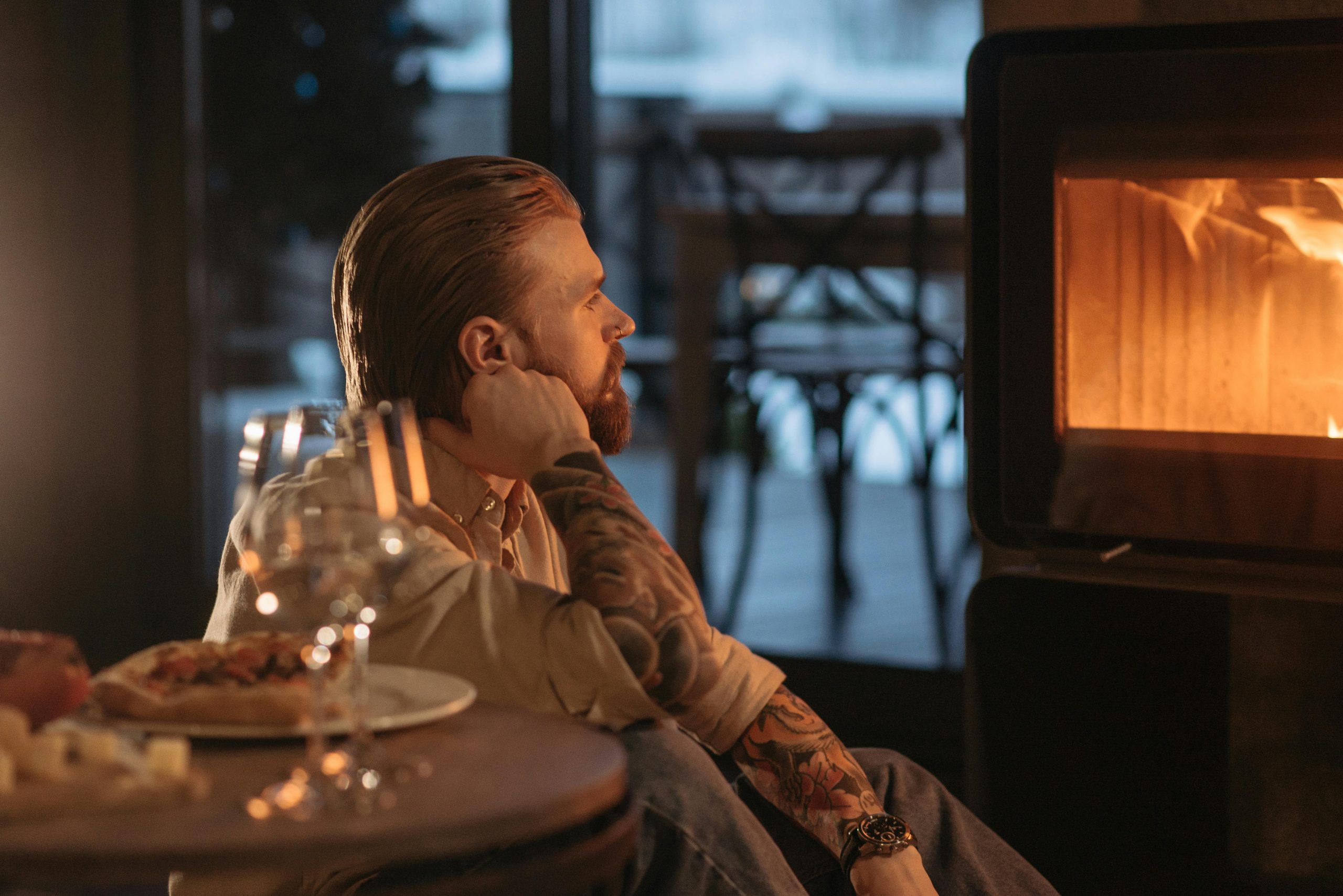 Homme avec des tatouages se détendant près de la cheminée, profitant d'une soirée cosy à l'intérieur