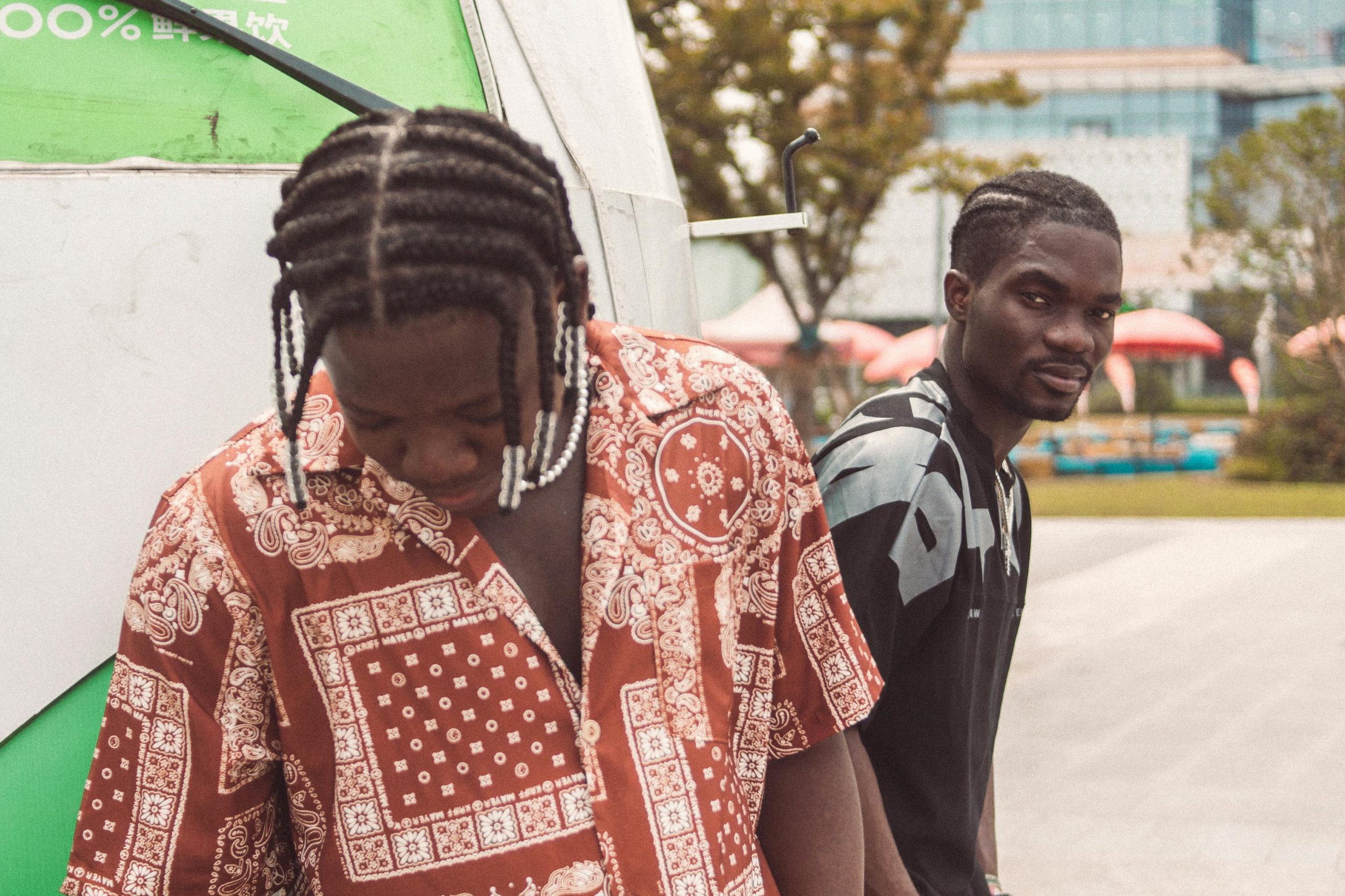 Two young African men with braids stand in Kumasi, Ghana, showcasing casual urban style. Deux jeunes hommes africains aux tresses se tiennent à Kumasi, au Ghana, affichant un style urbain décontracté.