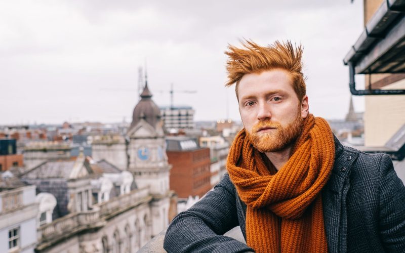 Homme roux à la barbe rousse et à l'écharpe orange sur un balcon en ville