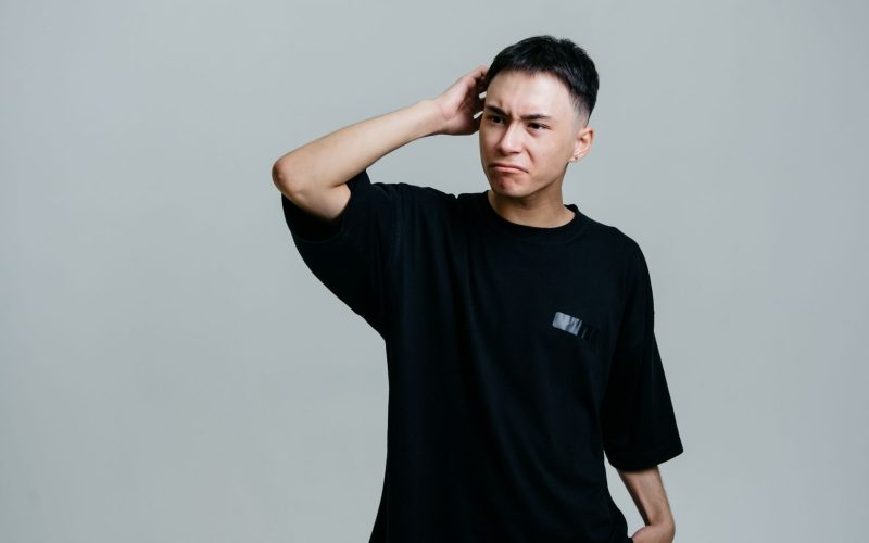 Jeune homme en tee-shirt noir qui se gratte la tête