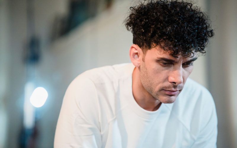 Homme aux cheveux bouclés en sweat blanc, regard vers le bas
