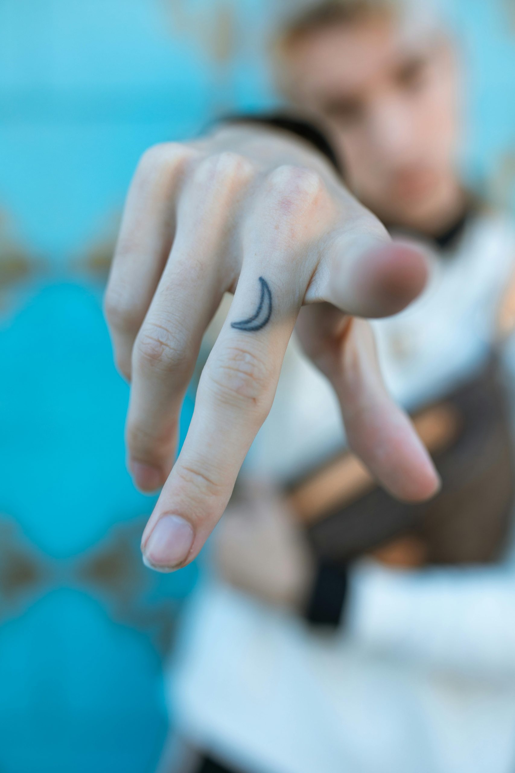 Pourquoi choisir un tatouage lune ? 1 Artistique gros plan d'un doigt avec un tatouage de lune sur un fond bleu flou.