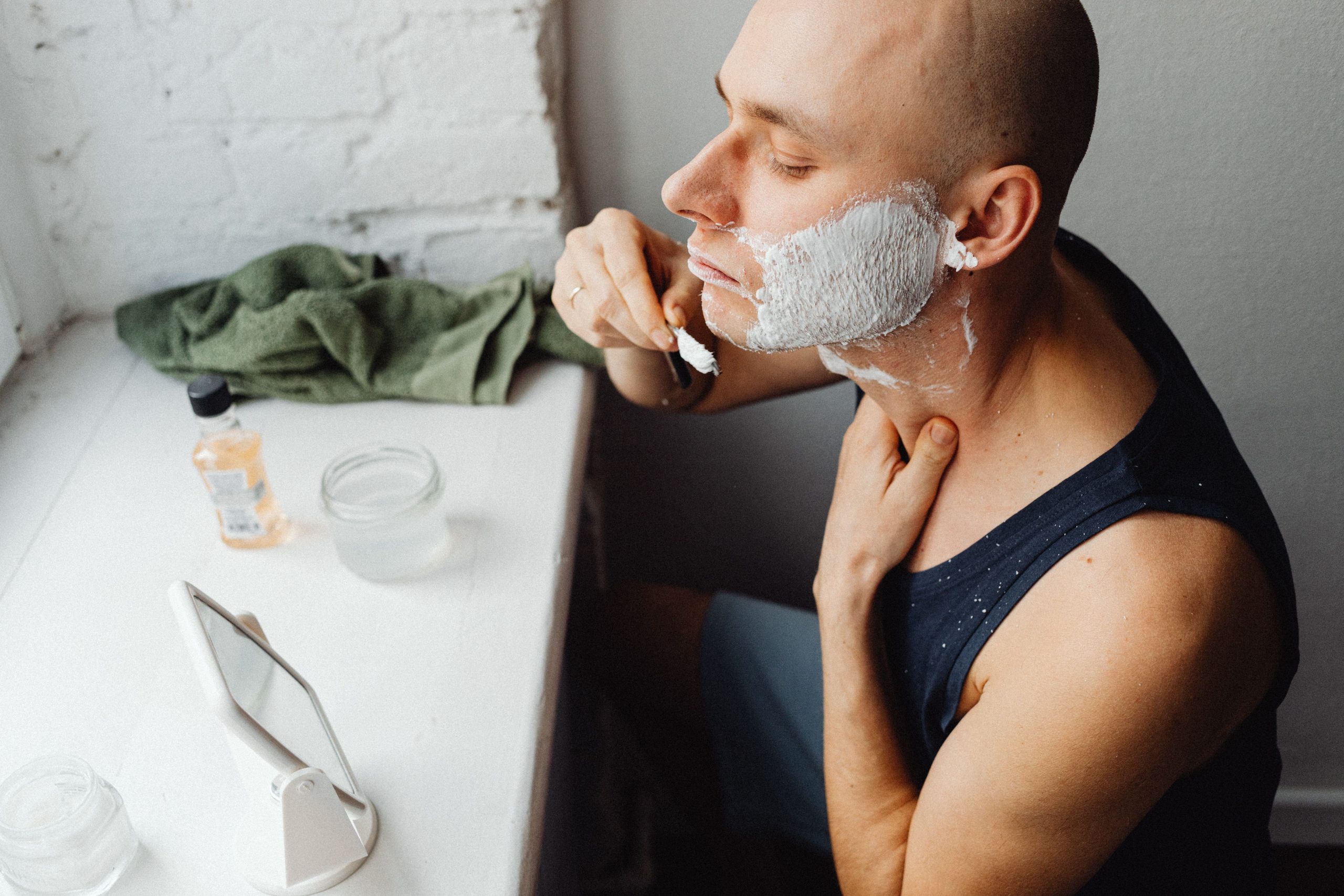 Comment bien porter sa barbe quand on a le crâne rasé ? 1 A man applying shaving cream while grooming in a bathroom at home. Un homme appliquant de la crème à raser tout en se toilettant dans une salle de bain à domicile.