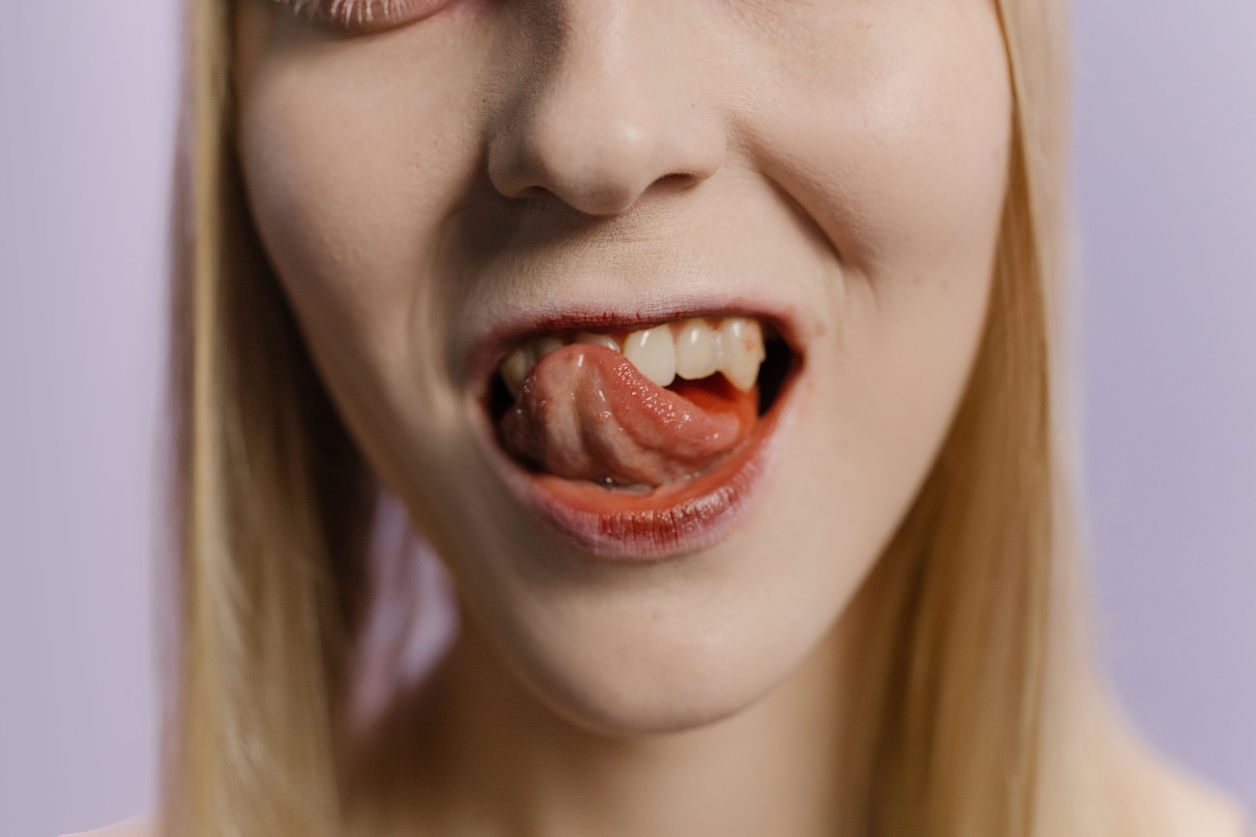 Quels remèdes naturels soulagent vraiment un bouton sur la langue ? 2 Close-up portrait of a blonde woman with her tongue out against a neutral background. Gros plan portrait d'une femme blonde avec la langue sortie sur un fond neutre.