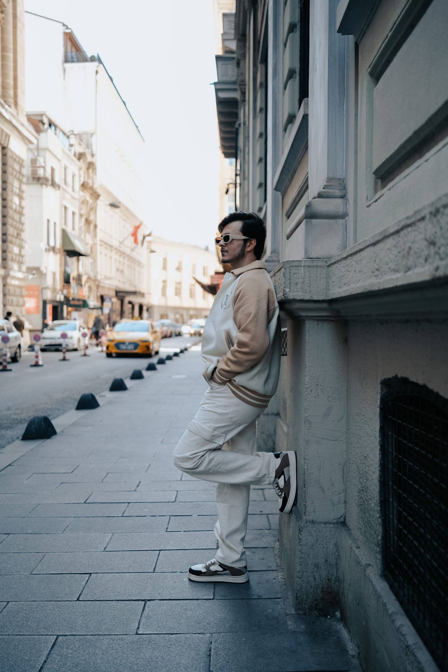 Fashionable man wearing sunglasses leans on a city street wall in a vibrant urban setting. Homme élégant portant des lunettes de soleil appuyé contre un mur de rue en ville dans un cadre urbain vibrant.