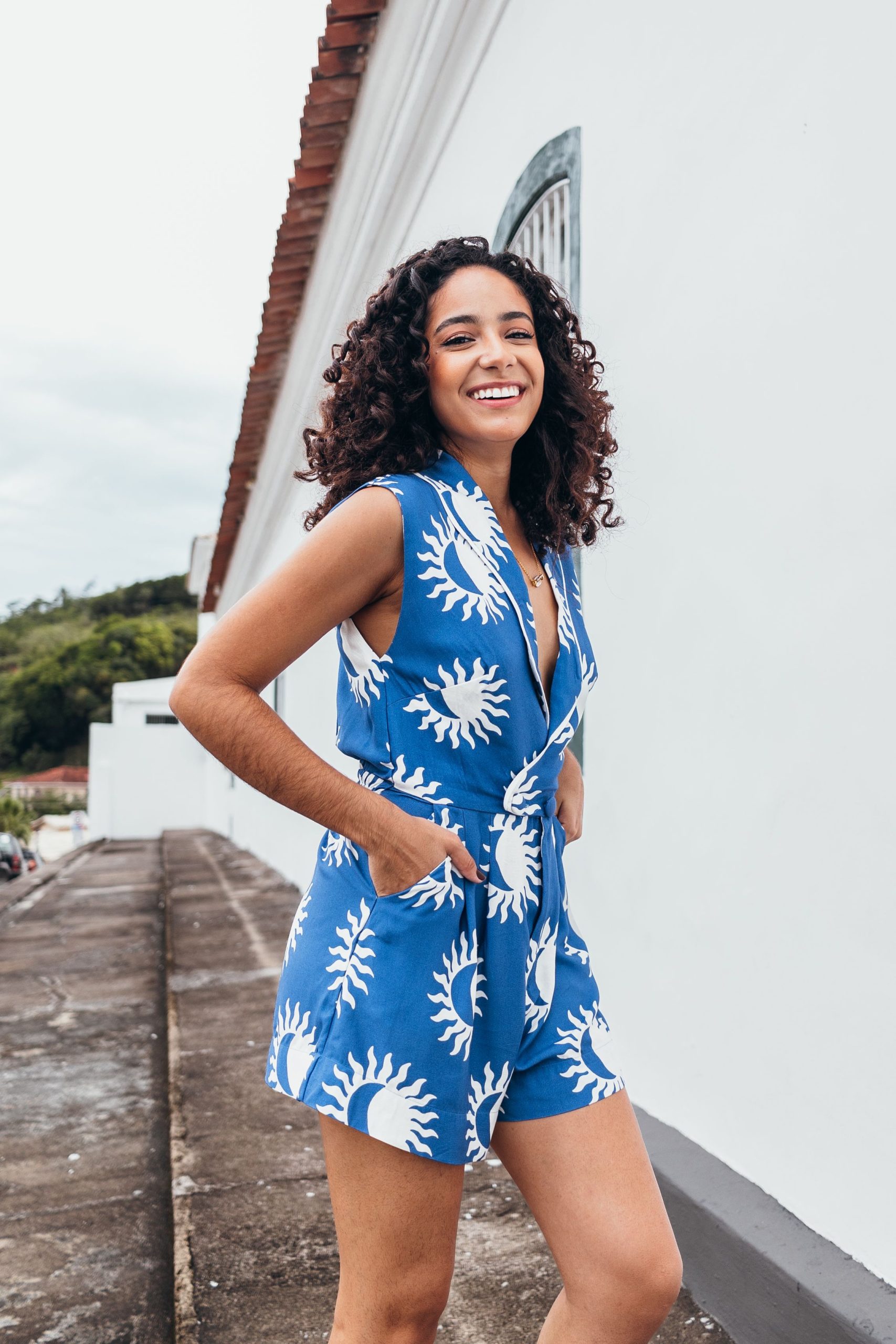 Femme souriante dans une combinaison-short bleue à motifs de soleil profitant d'un cadre extérieur lumineux.