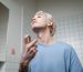 A stylish young man applying perfume in a contemporary bathroom setting, embracing a metrosexual lifestyle. Un jeune homme élégant appliquant du parfum dans une salle de bain contemporaine, embrassant un style de vie métrosexuel.