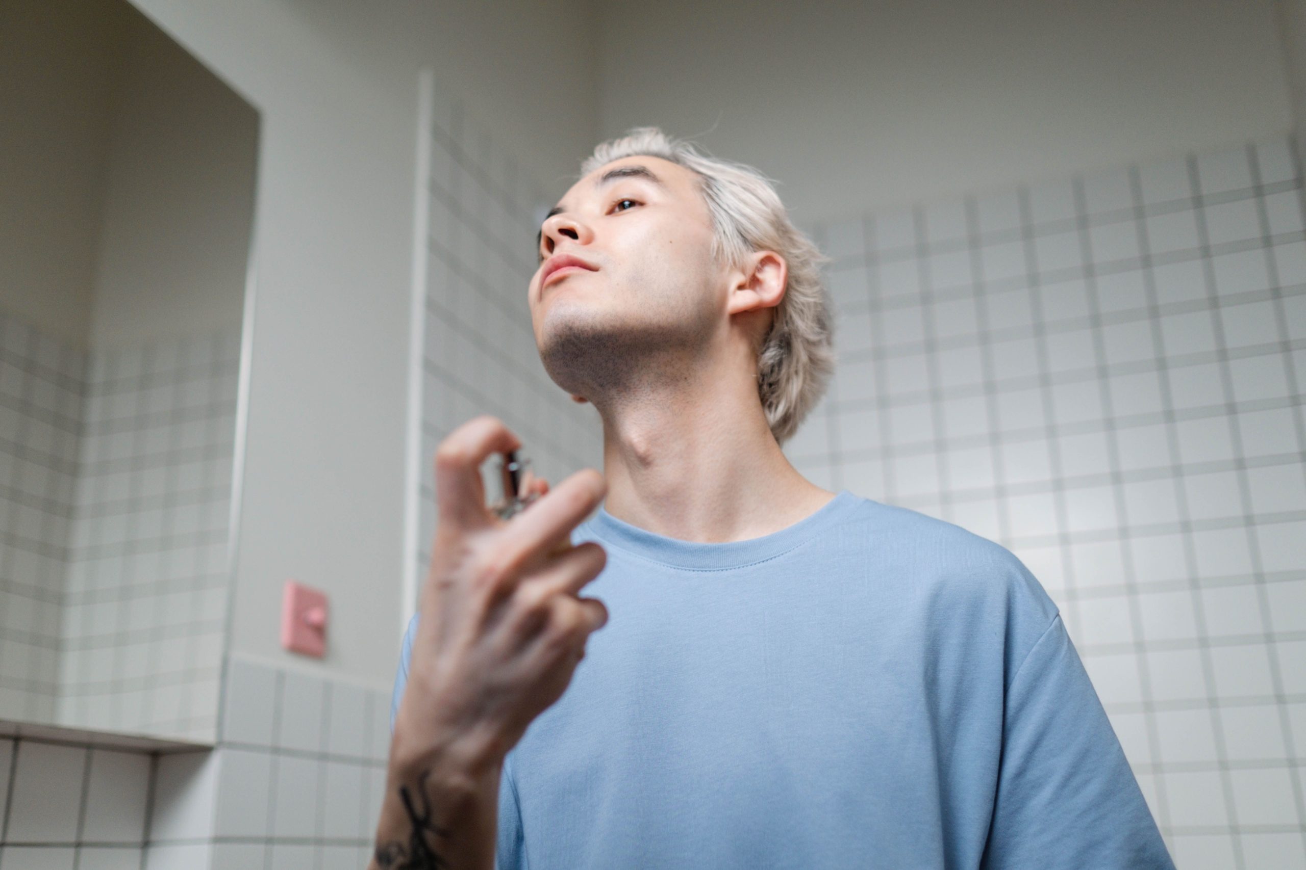 A stylish young man applying perfume in a contemporary bathroom setting, embracing a metrosexual lifestyle. Un jeune homme élégant appliquant du parfum dans une salle de bain contemporaine, embrassant un style de vie métrosexuel.