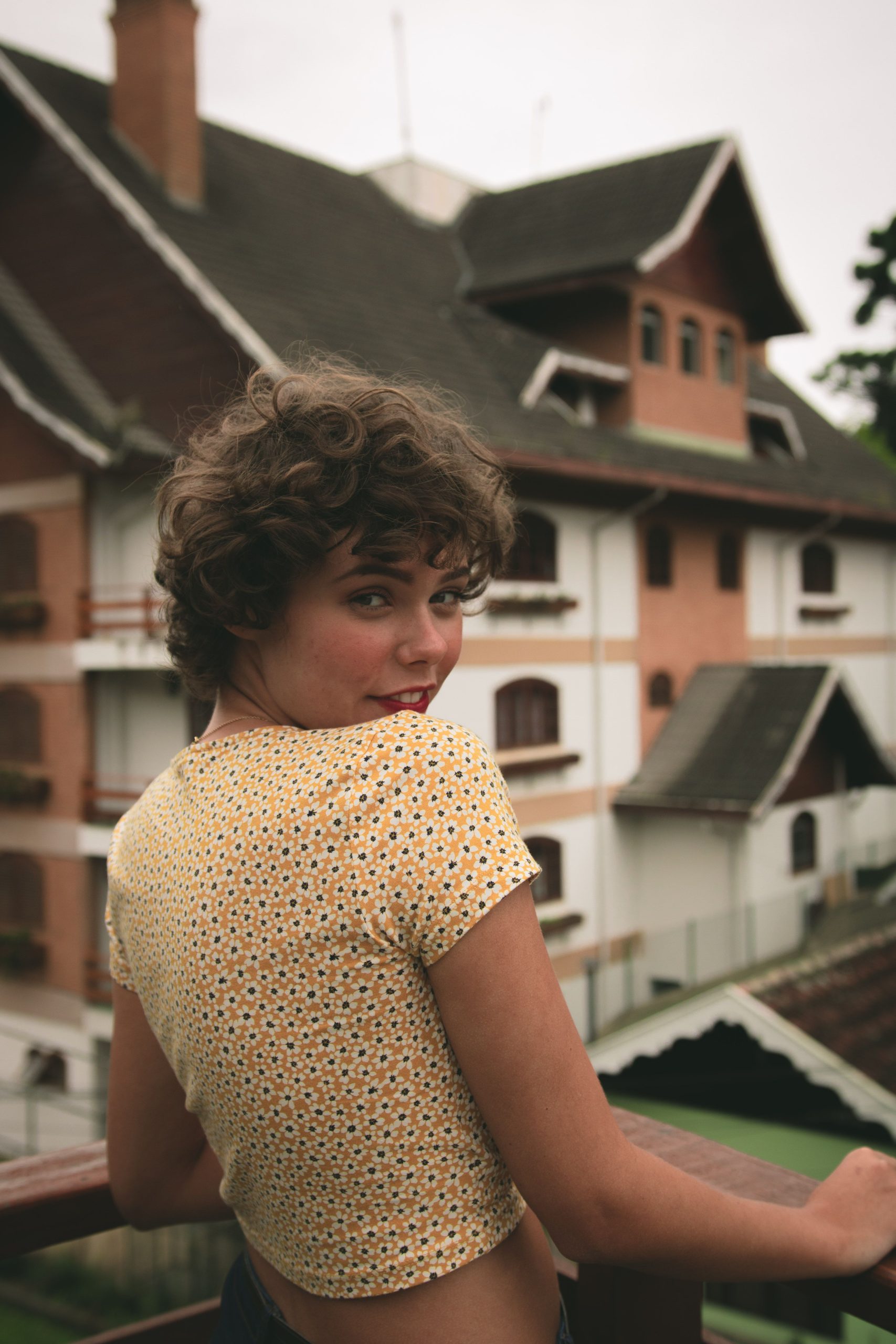 Comment entretenir une coupe courte pour cheveux frisés ? 4 A young woman with curly hair smiling and posing by a stylish building in daylight. Une jeune femme aux cheveux bouclés souriante posant devant un bâtiment élégant en plein jour.