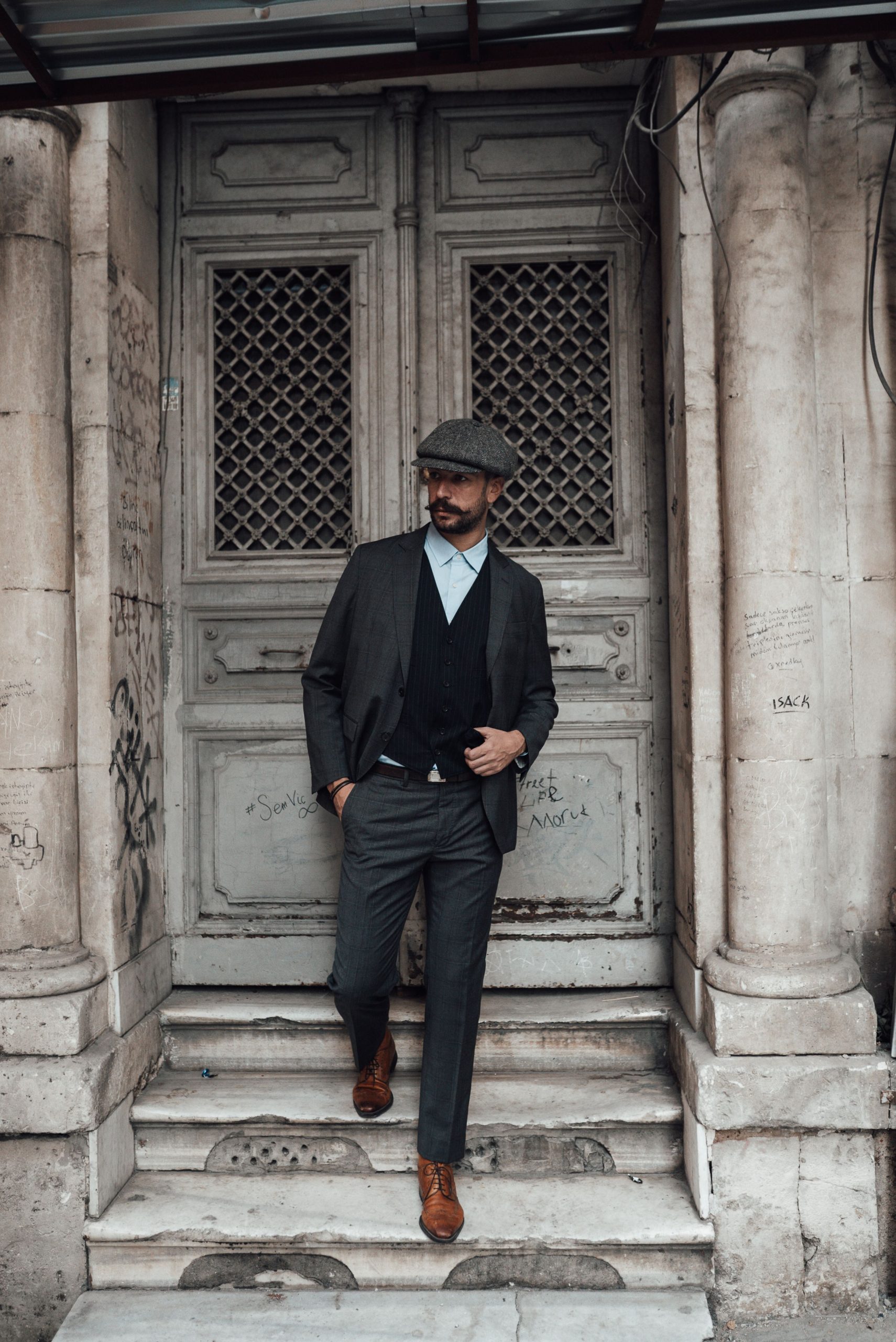 Comment habiller classe en homme sans se ruiner ? 9 Full body of confident man in stylish formal suit standing with hand in pocket near aged door of building in daylight Homme de plein pied en costume formel élégant et confiant, debout la main dans la poche près de la porte vieillie d'un bâtiment en plein jour