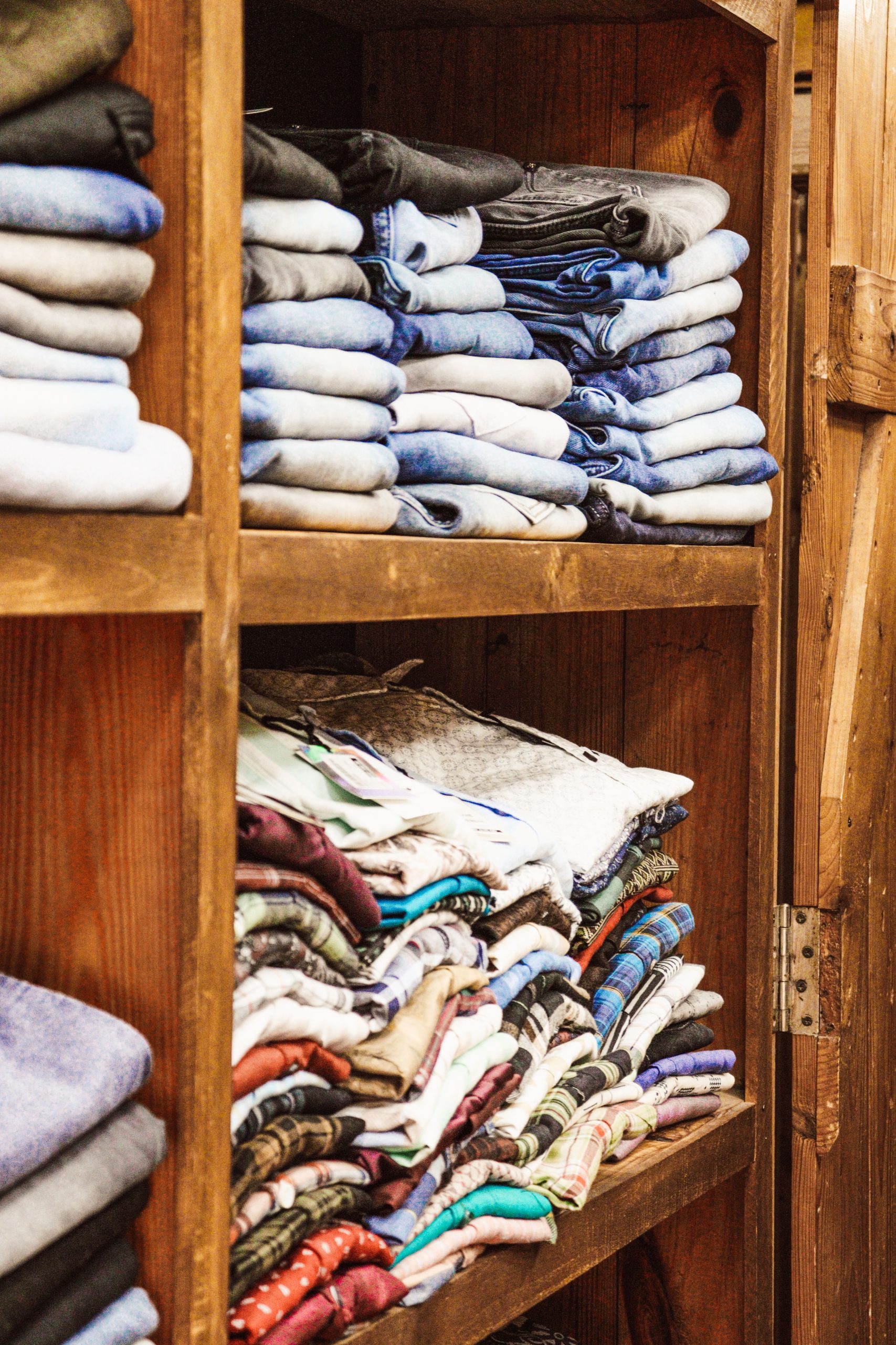 Neatly folded clothes on wooden shelves, showcasing diverse colors and fabric textures. Vêtements soigneusement pliés sur des étagères en bois, mettant en avant des couleurs et des textures de tissus variées.