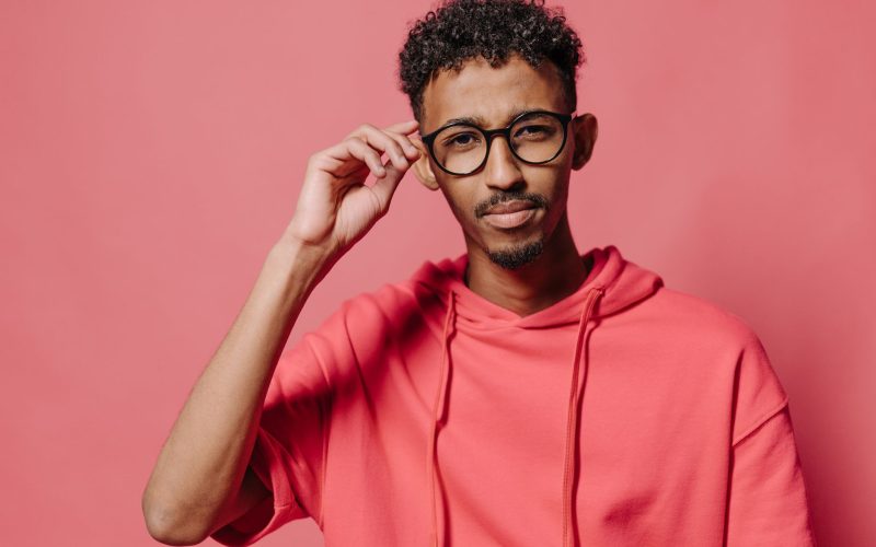 Homme aux cheveux frisés coupés court, lunettes et sweat rose