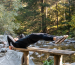 Man performing a core exercise on a bench by a serene river in a forest setting. Homme effectuant un exercice de base sur un banc près d'une rivière sereine dans un cadre forestier.