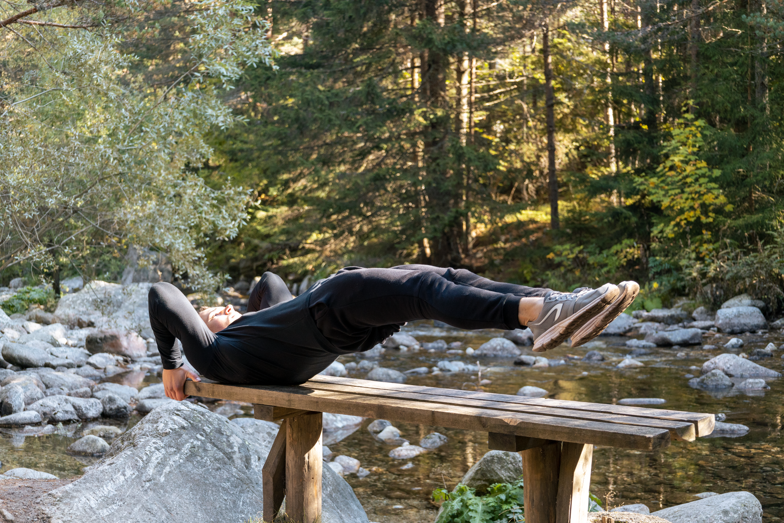 Quels exercices de musculation du dos vraiment fonctionnent ? 1 Man performing a core exercise on a bench by a serene river in a forest setting. Homme effectuant un exercice de base sur un banc près d'une rivière sereine dans un cadre forestier.