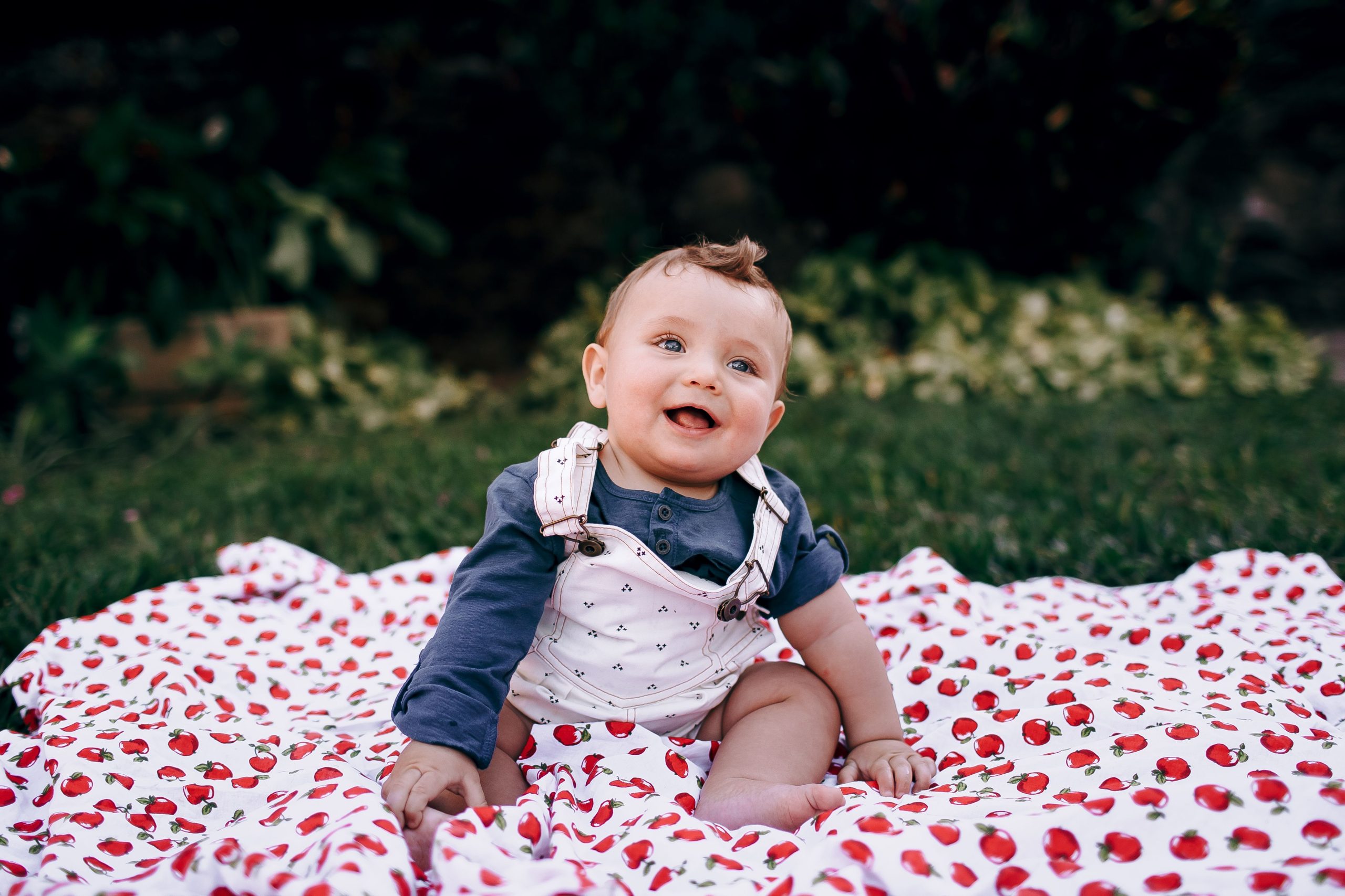 Quels sont les prénoms américains pour garçons les plus populaires ? 8 A happy baby sitting on a cherry-printed blanket outdoors, enjoying a sunny day. Un bébé heureux assis sur une couverture imprimée de cerises à l'extérieur, profitant d'une journée ensoleillée.