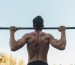 Rear view of a strong man exercising shirtless with a barbell outdoors, showcasing strength and fitness. Vue arrière d'un homme musclé faisant de l'exercice sans chemise avec un haltère à l'extérieur, mettant en avant la force et la condition physique.