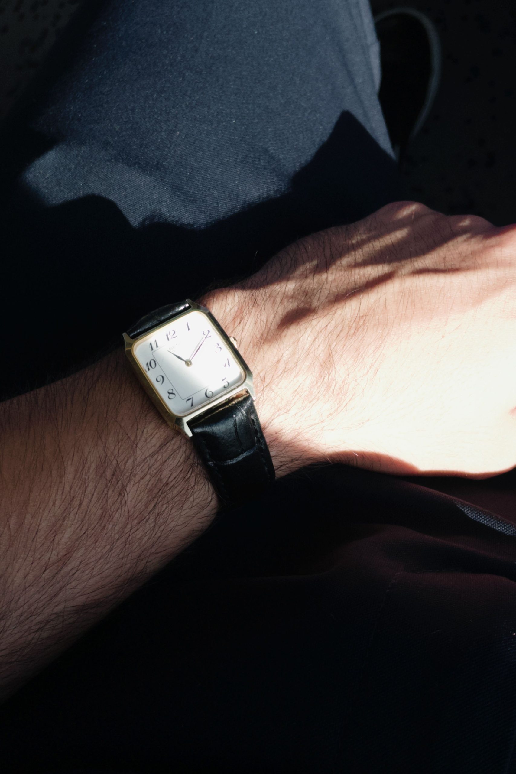 Quelle montre carrée pour homme choisir vraiment ? 6 Stylish square wristwatch with leather band on wrist, captured in sunlight. Montre-bracelet carrée élégante avec bracelet en cuir au poignet, capturée à la lumière du soleil.