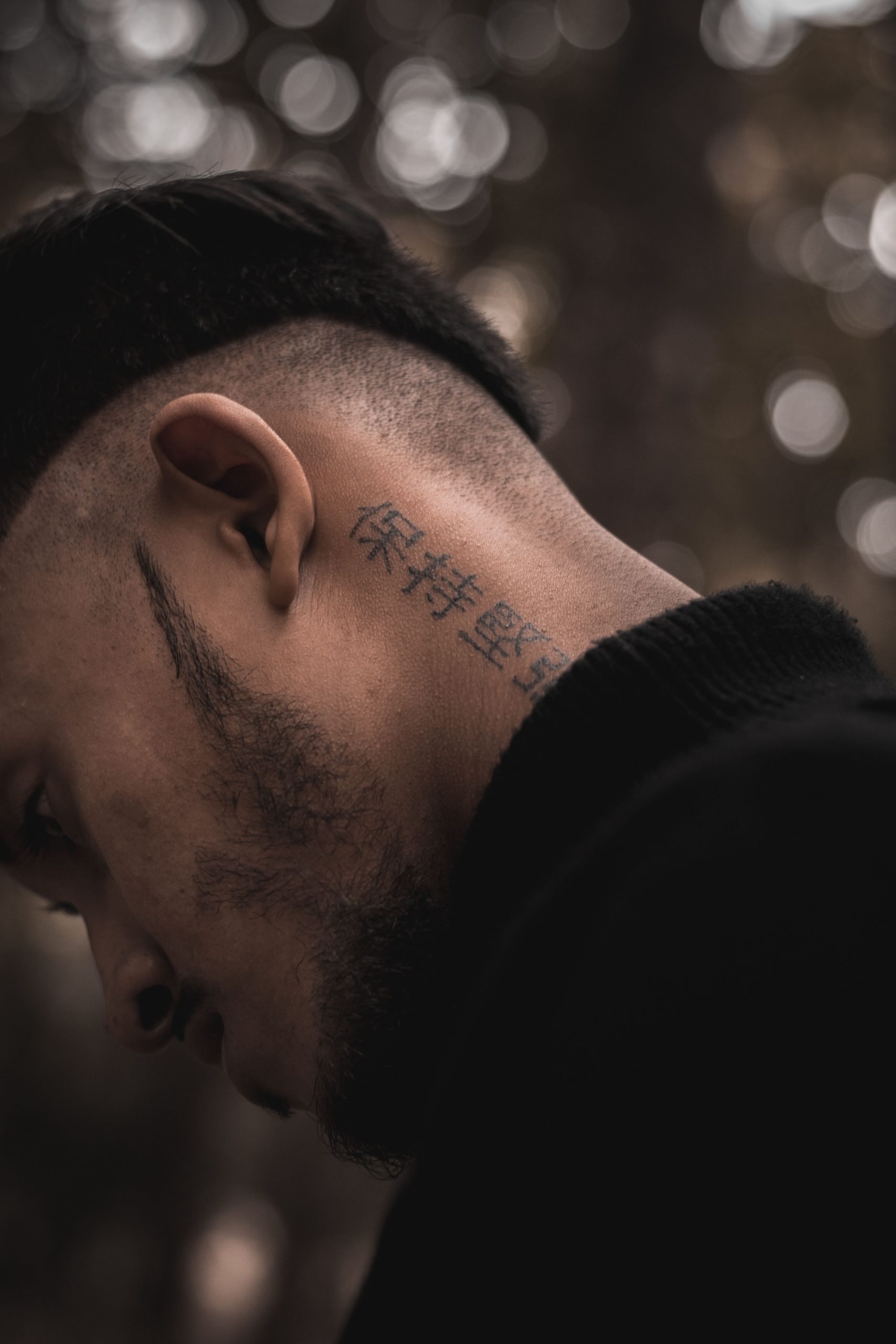 Pourquoi choisir un tatouage dans le cou quand on est homme ? 5 Close-up portrait of a tattooed man in profile view, highlighting neck tattoos and artistic expression. Portrait en gros plan d'un homme tatoué en vue de profil, mettant en évidence les tatouages du cou et l'expression artistique.