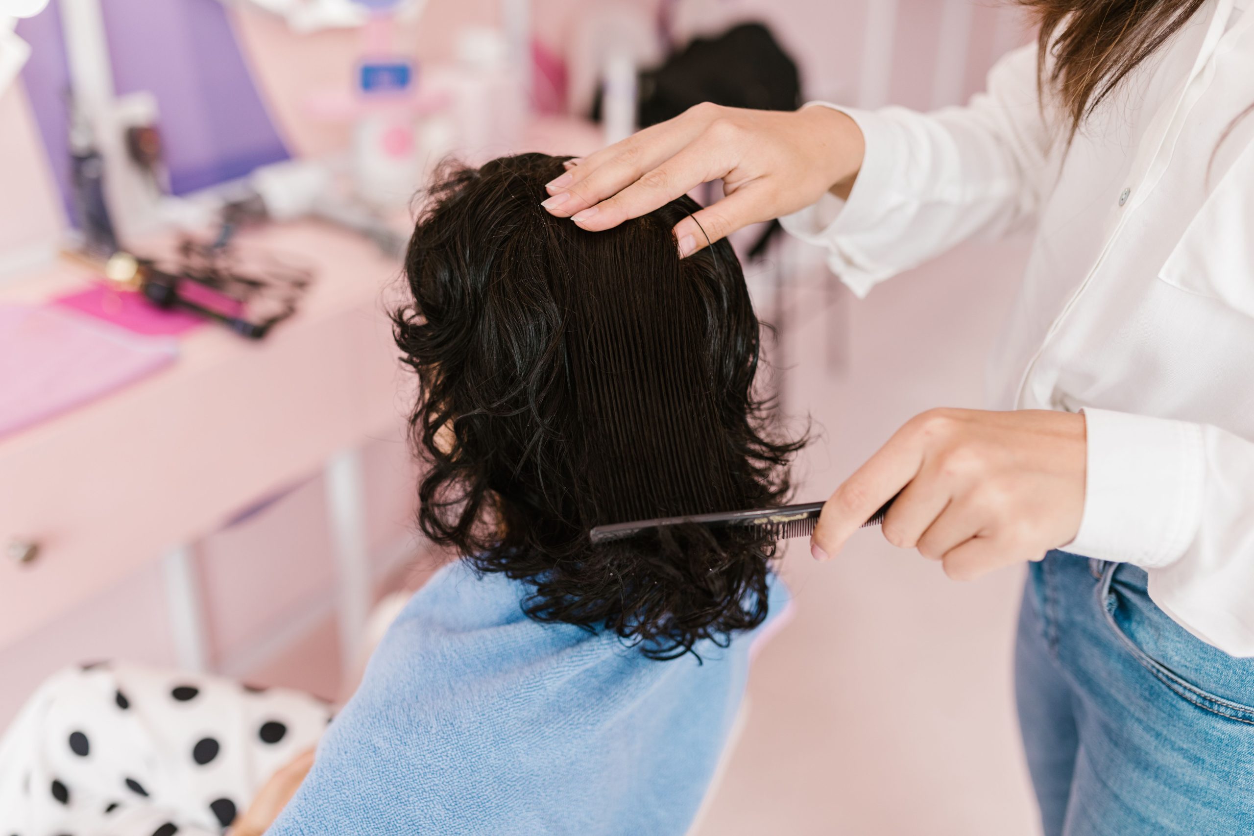 Quelle coupe choisir pour cheveux ondulés et épais ? 1 Close-up of a woman receiving hairstyling treatment in a contemporary salon. Gros plan d'une femme recevant un traitement de coiffure dans un salon contemporain.