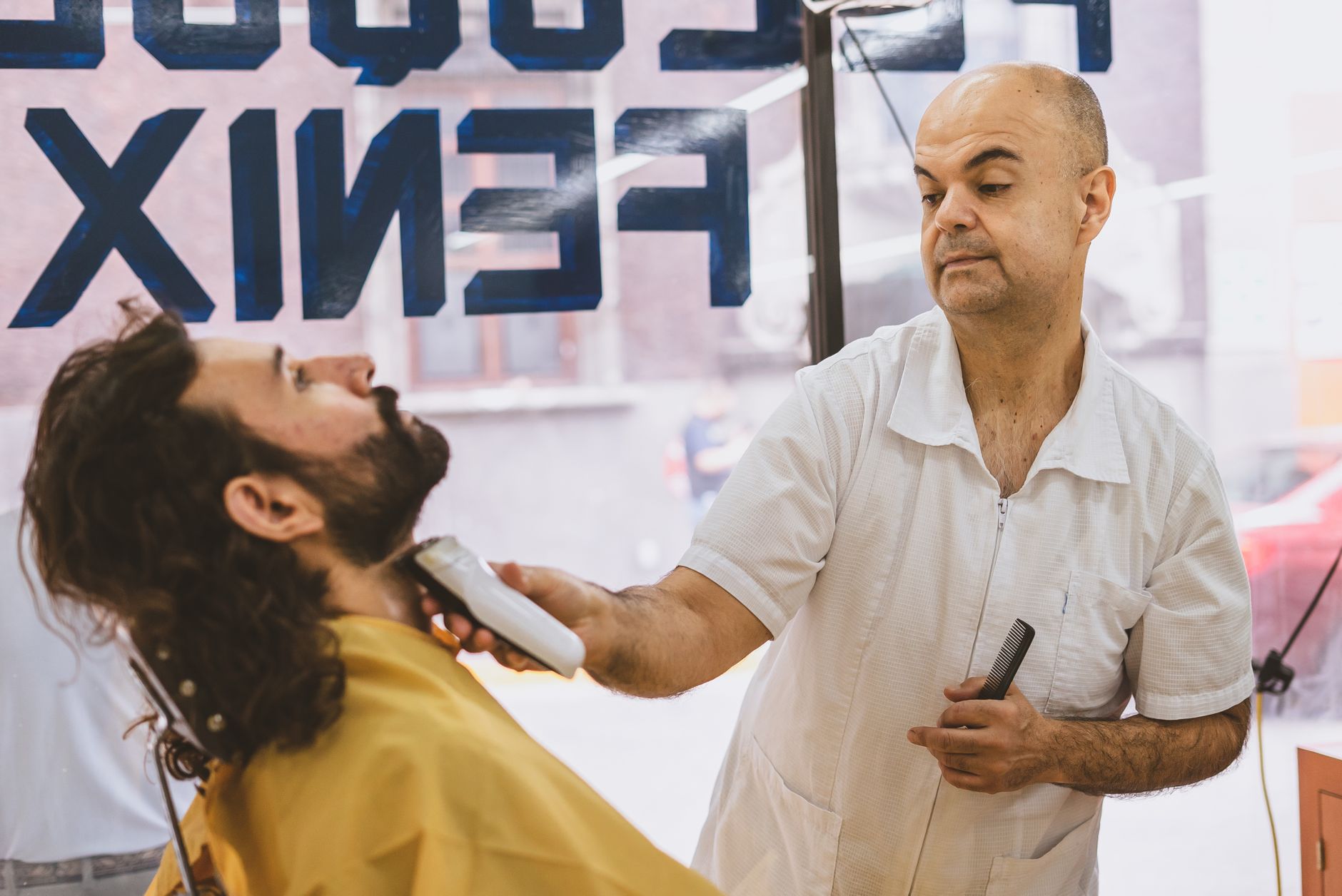 Barbier qui taille la barbe d'un client aux cheveux longs et bouclés