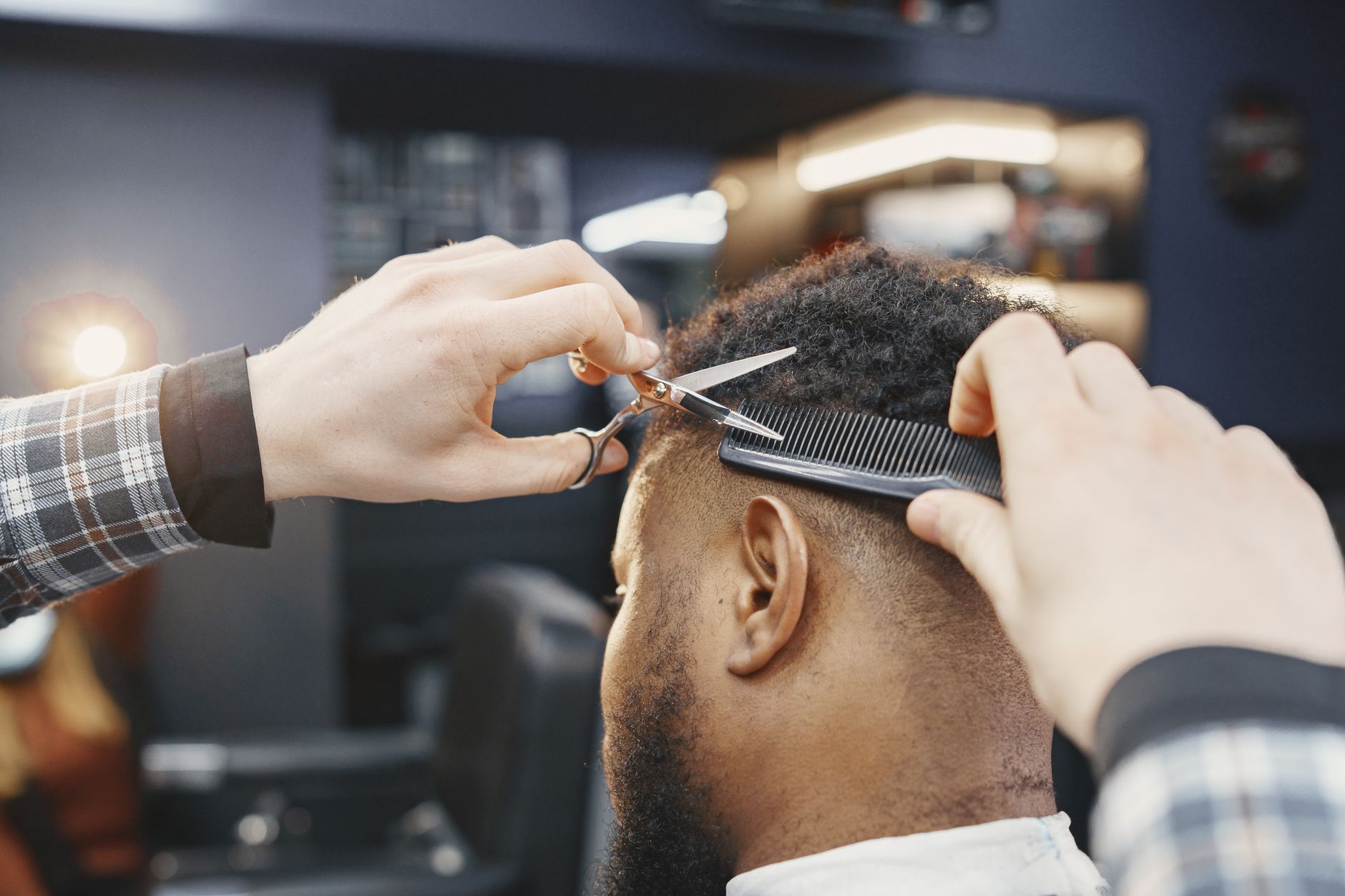 Coiffeur qui coupe aux ciseaux les cheveux bouclés d'un client