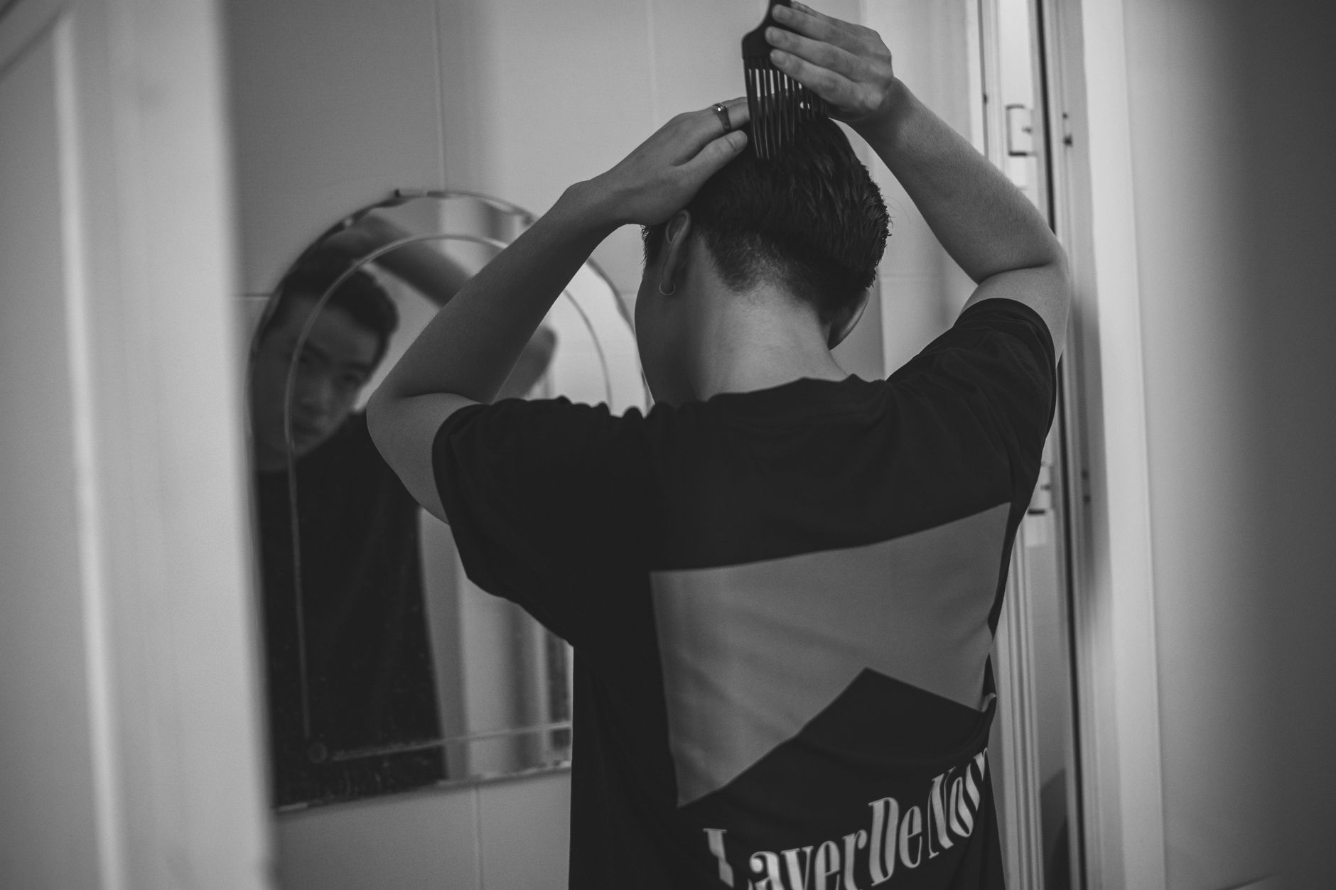 Cheveux gras homme : arrête ces gestes qui aggravent tout 2 Homme qui coiffe ses cheveux devant un miroir