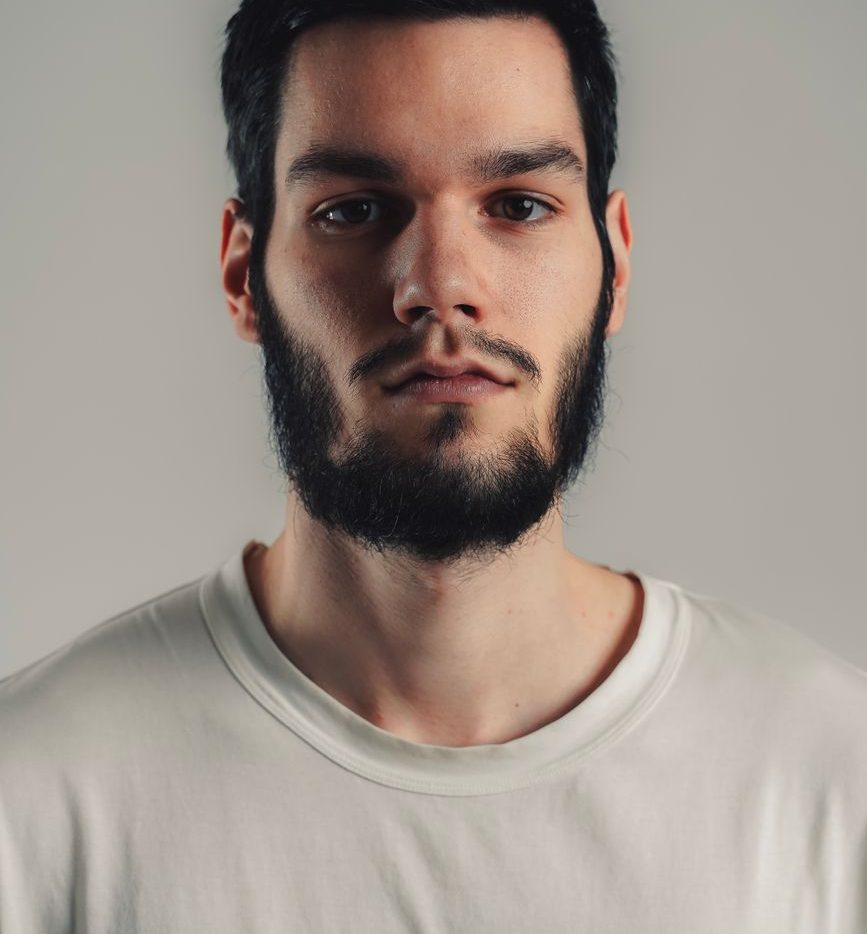 Homme de face avec un collier de barbe noir, joues rasées et moustache légère