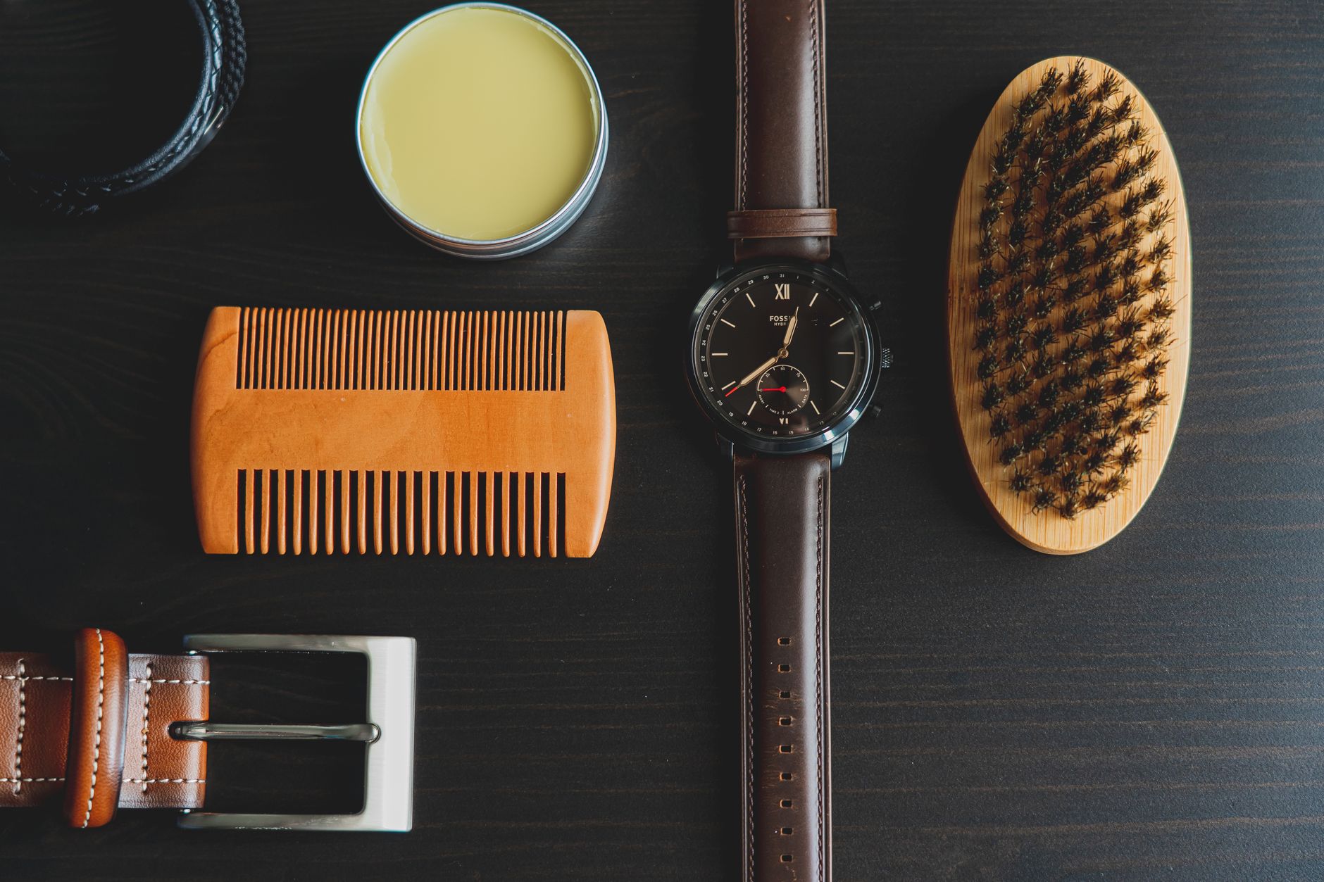 Peigne en bois, pot de cire et brosse posés sur une table sombre