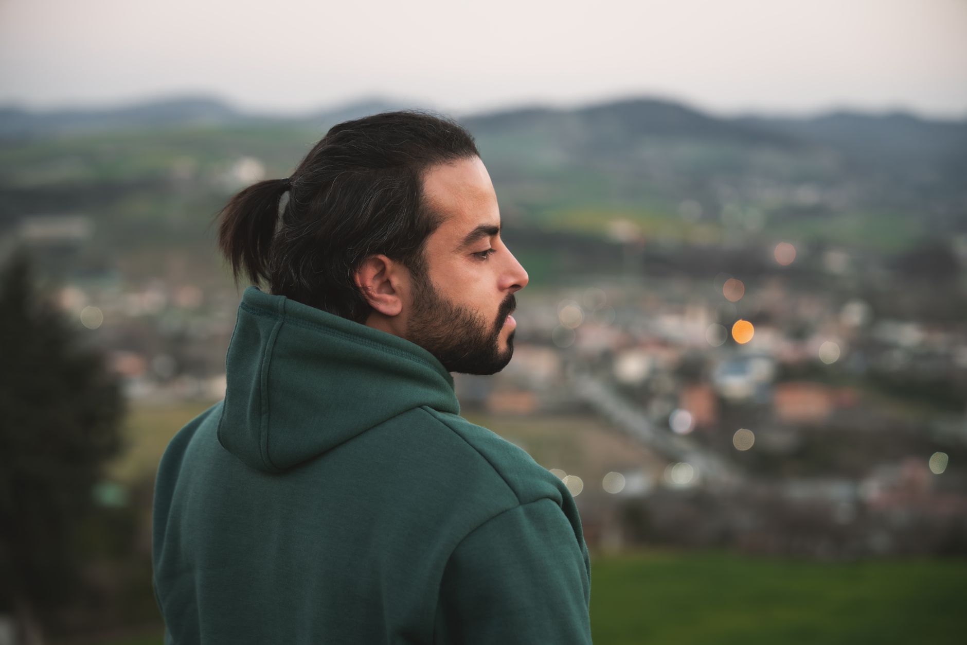 Homme barbu de profil aux cheveux attachés en queue, sweat vert
