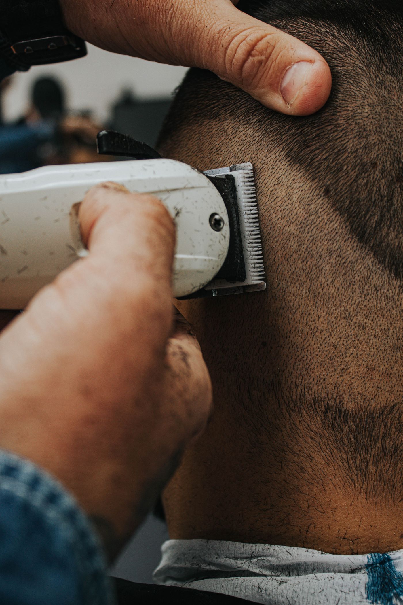Tondeuse blanche reprenant la nuque d'un client, main du barbier posée sur le crâne