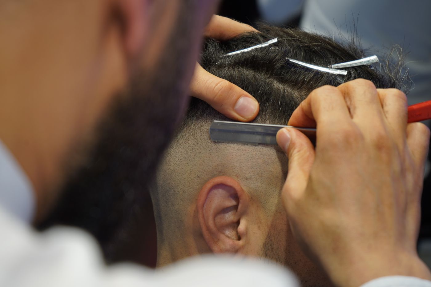 Barbier traçant au rasoir la limite d'un fondu au-dessus de l'oreille, mèches du dessus pincées