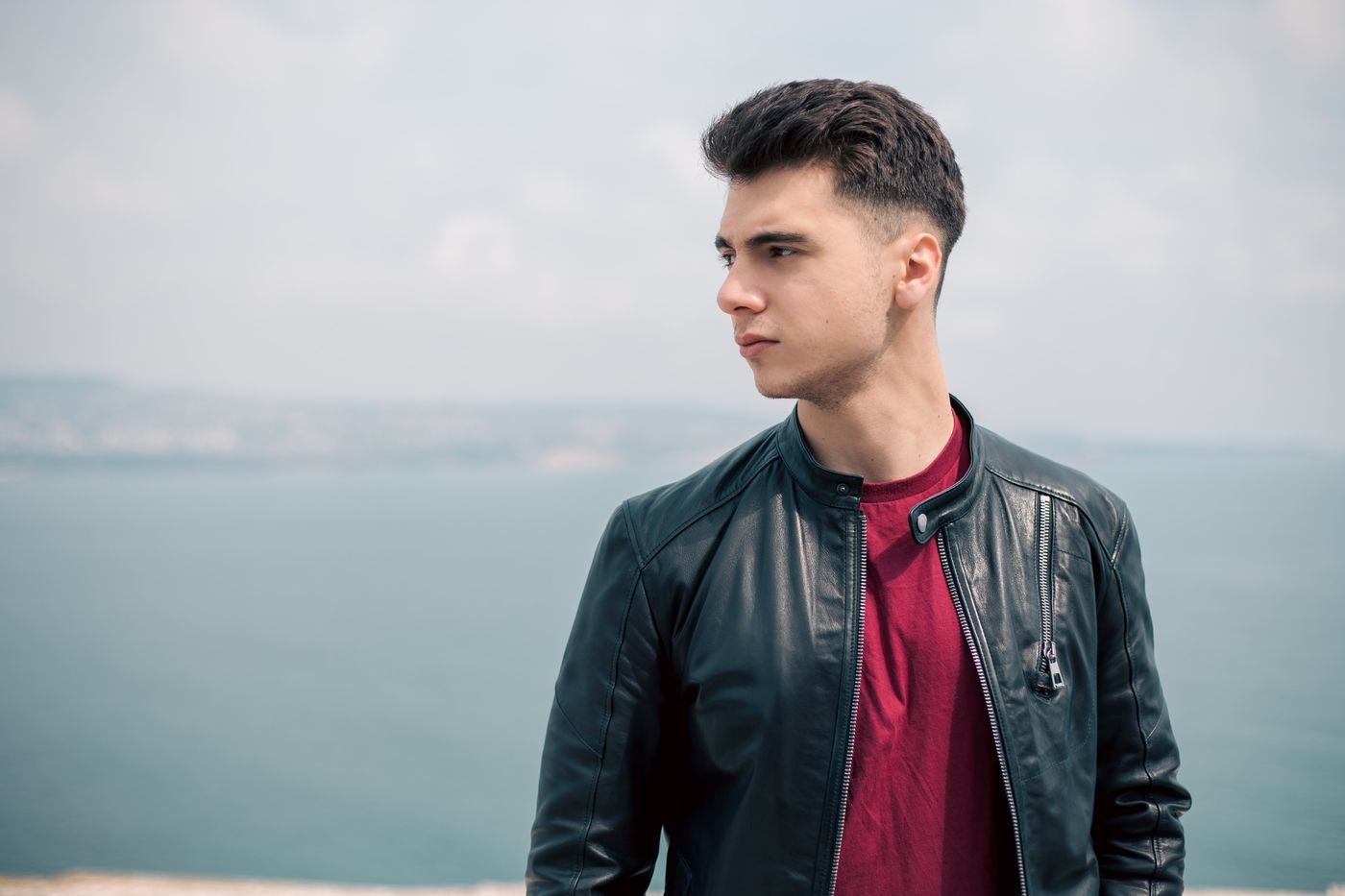 Jeune homme en blouson de cuir, dessus relevé et côtés fondus, face à la mer