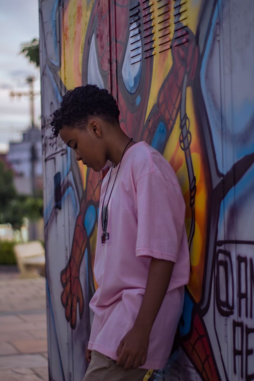 Adolescent aux cheveux mi-longs, adossé à un mur peint