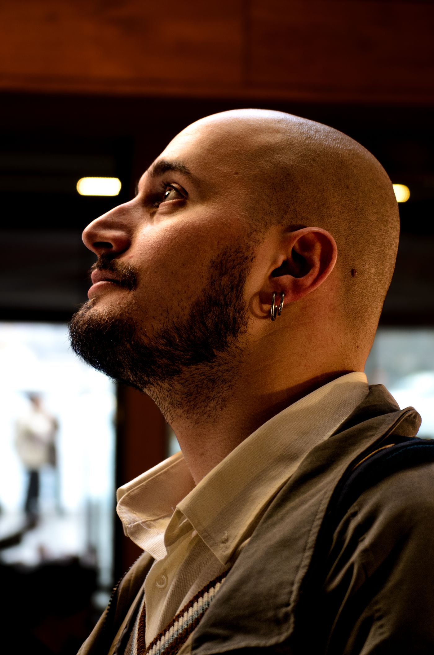 Homme au crâne tondu presque à blanc et barbe courte, de profil, regard levé