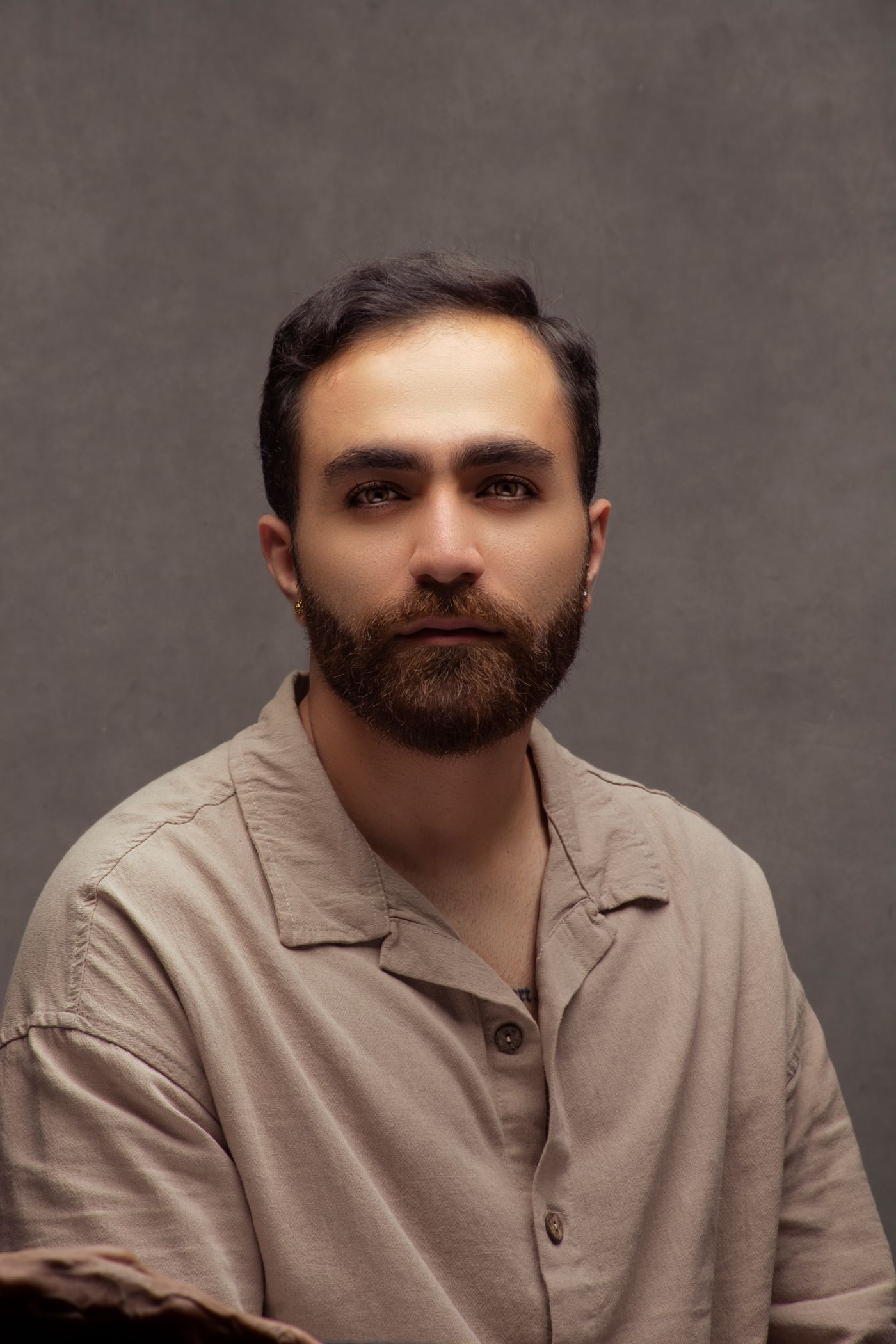 Homme de face à la barbe brune taillée courte et dense, sur fond gris neutre