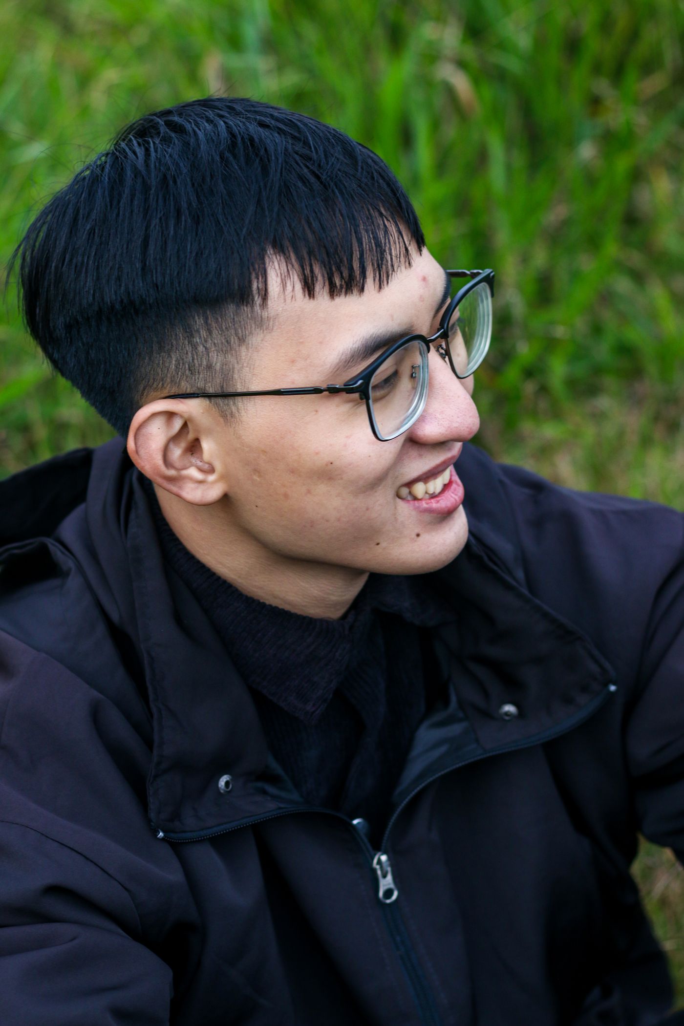 Jeune homme à lunettes souriant, coupe au bol à frange droite effilée et côtés rasés