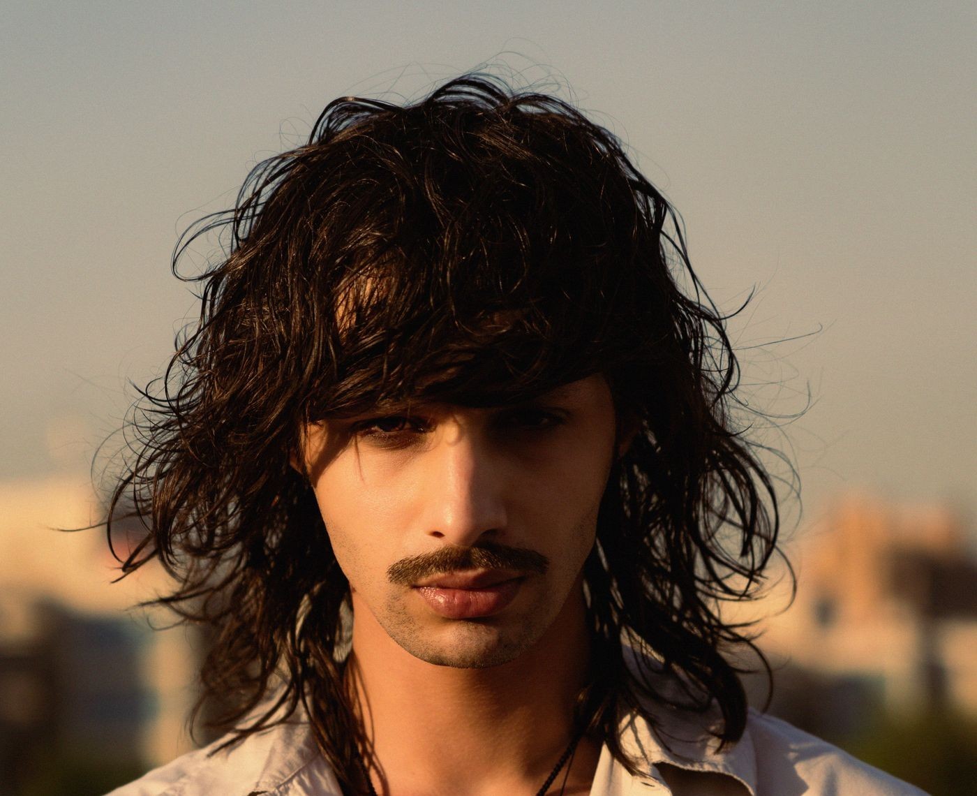 Homme moustachu aux cheveux mi-longs en couches effilées, frange tombant sur les yeux