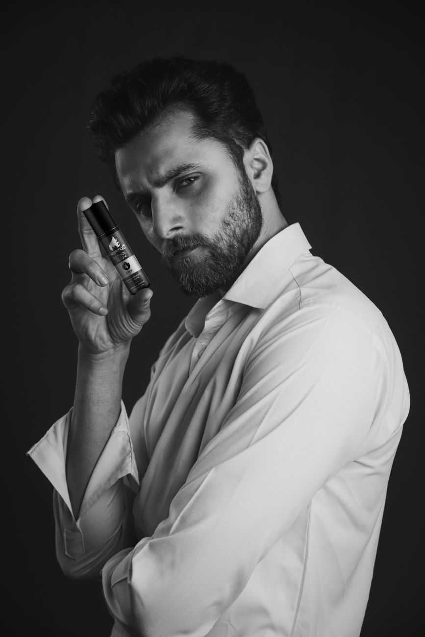 Homme barbu qui tient un flacon d'huile près du visage, en noir et blanc