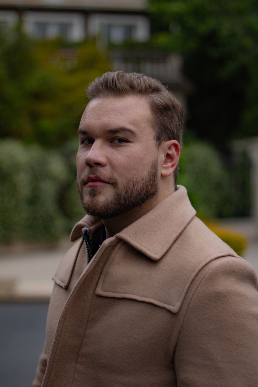 Homme à la barbe courte et soignée, manteau camel, de trois quarts