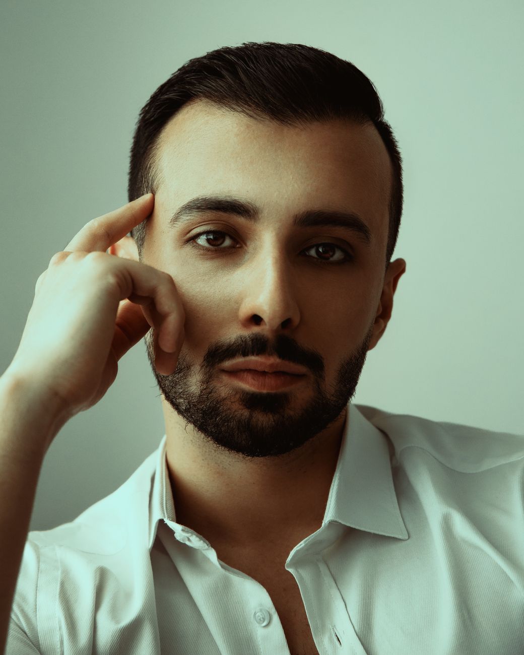 Homme à la barbe courte taillée net, main sur la tempe, chemise blanche