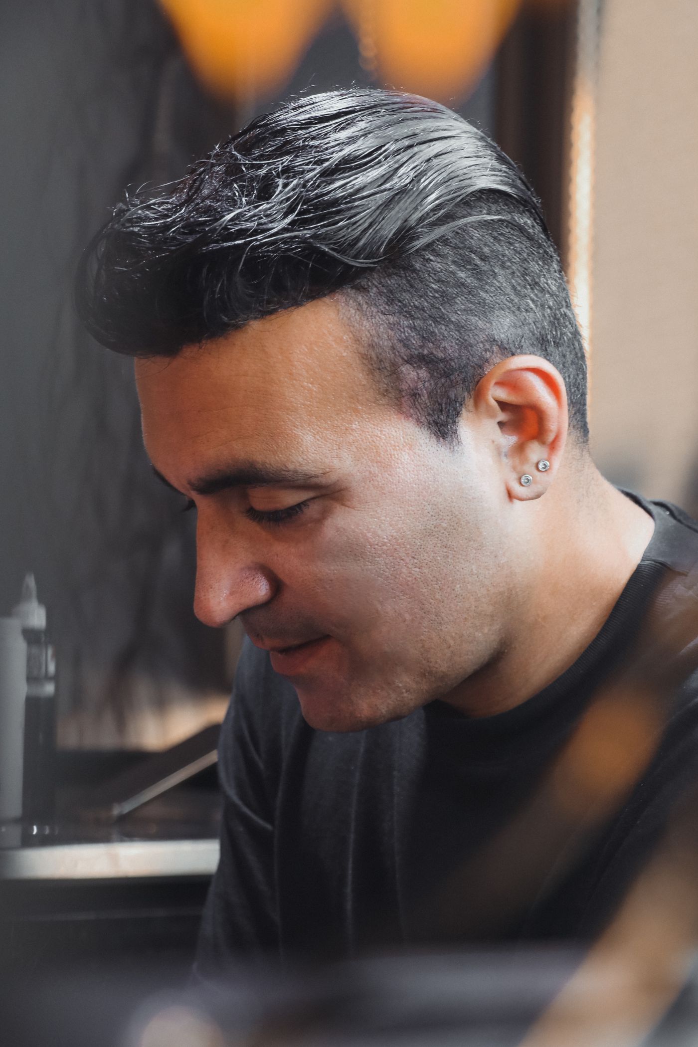 Homme brun aux cheveux mi-longs mouillés coiffés en arrière, côtés tondus au-dessus de l'oreille