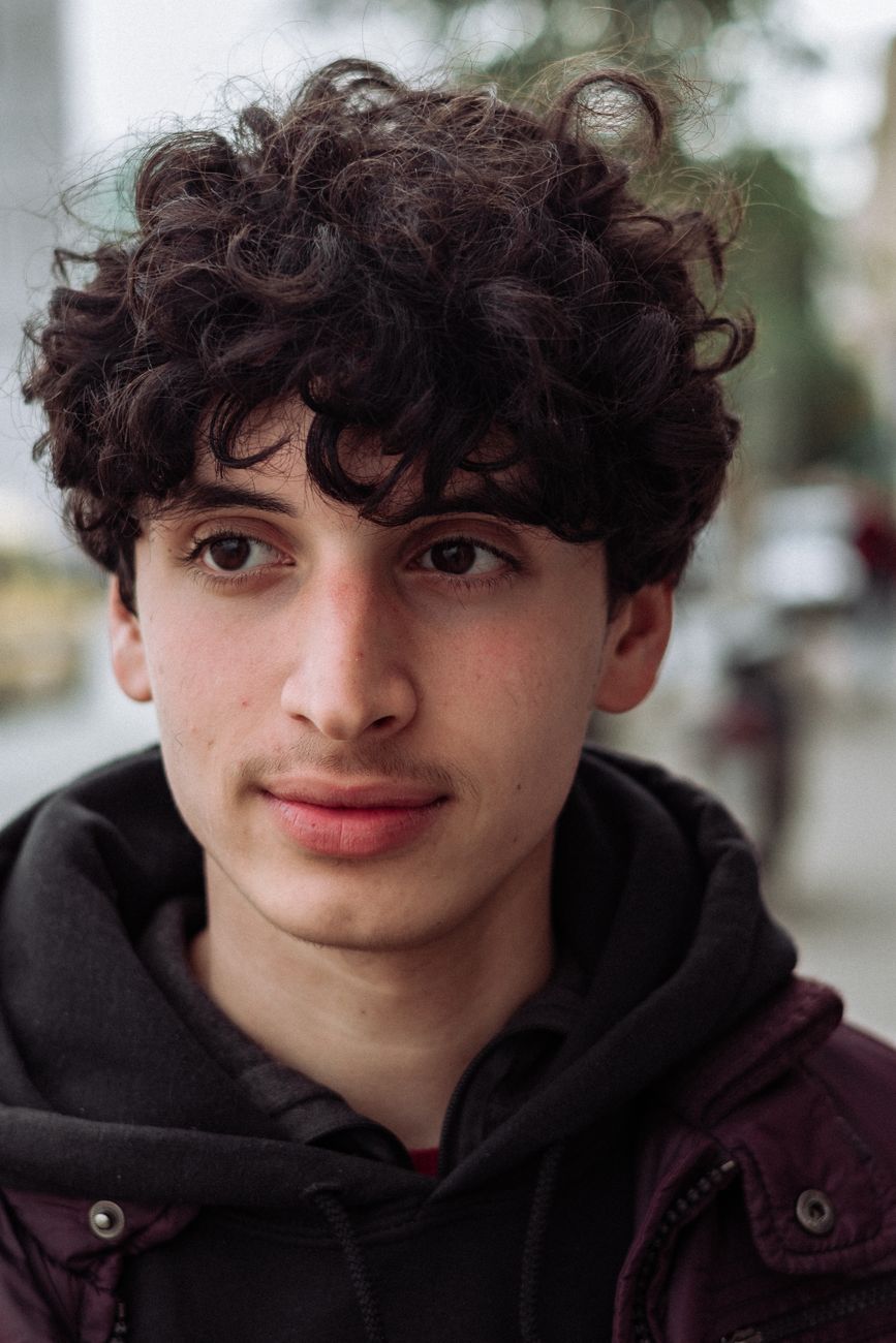 Jeune homme aux boucles qui retombent sur le front, sweat sombre