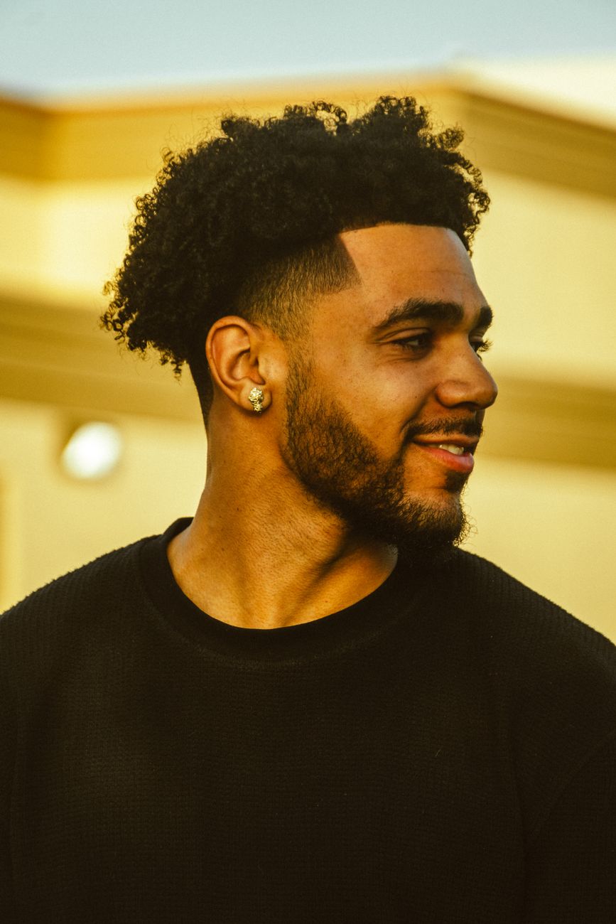 Homme souriant au dessus bouclé court et au contour net, de trois quarts