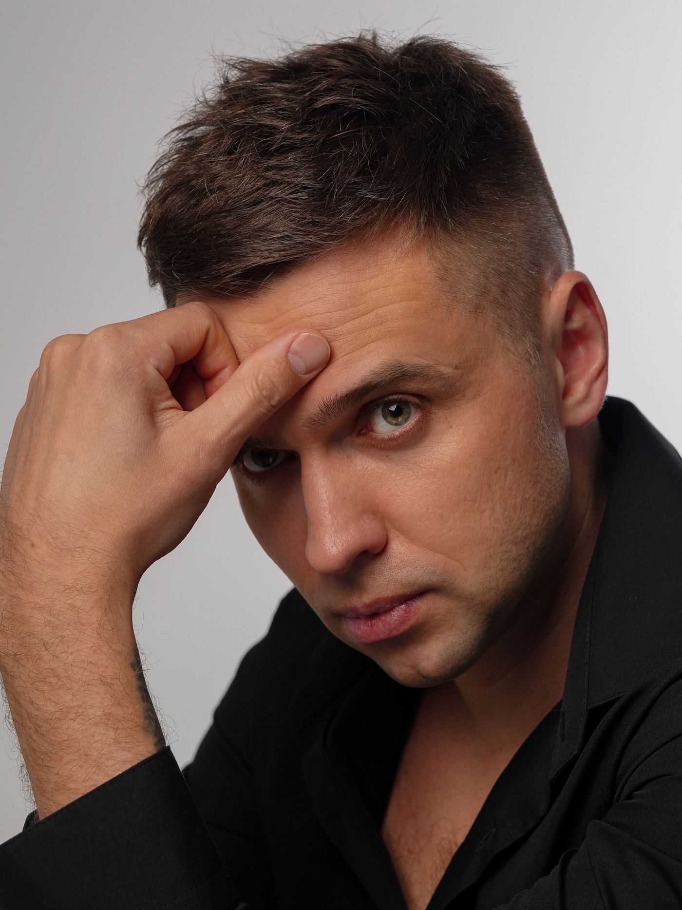 Homme brun à la coupe courte en brosse, côtés dégradés, main posée sur le front
