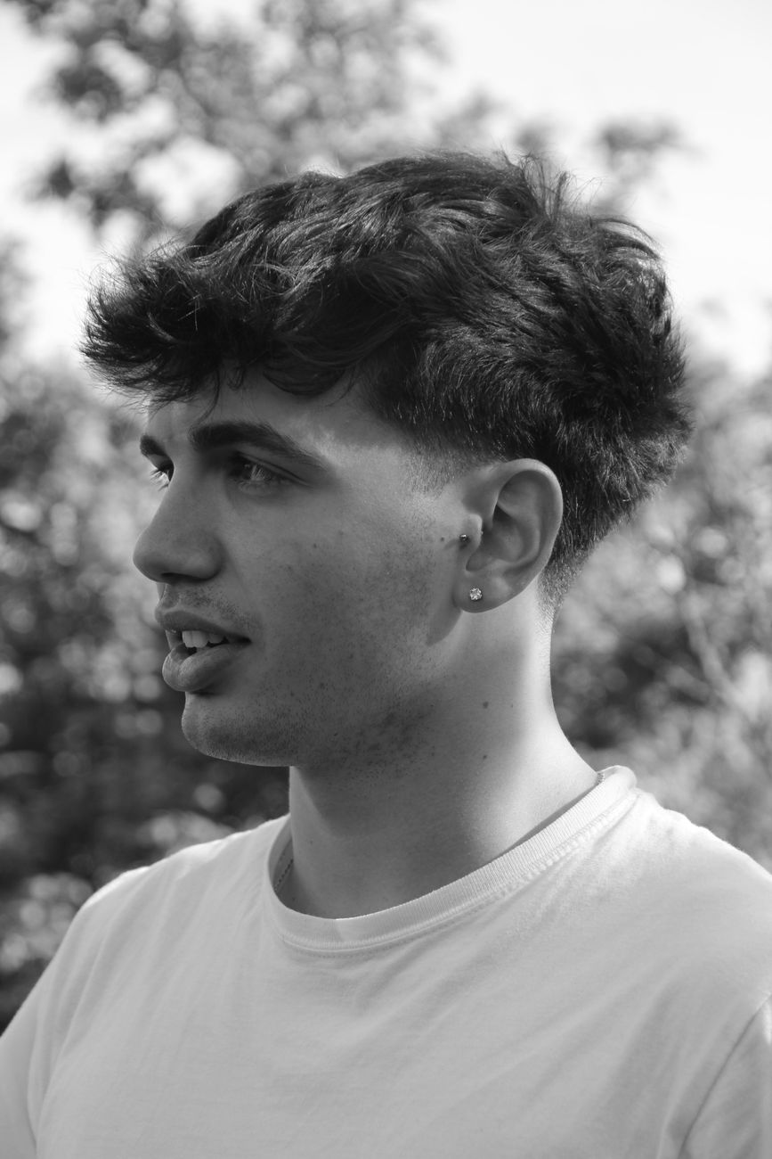 Jeune homme de profil, dessus texturé ramené vers l'avant et côtés dégradés, en noir et blanc