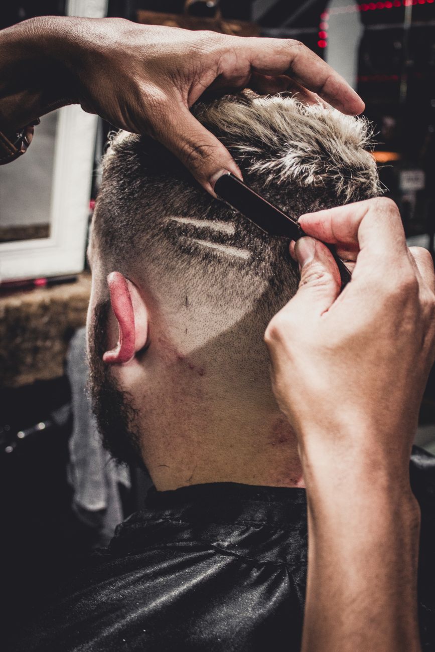 Barbier qui dessine deux traits rasés sur le côté d'un dégradé