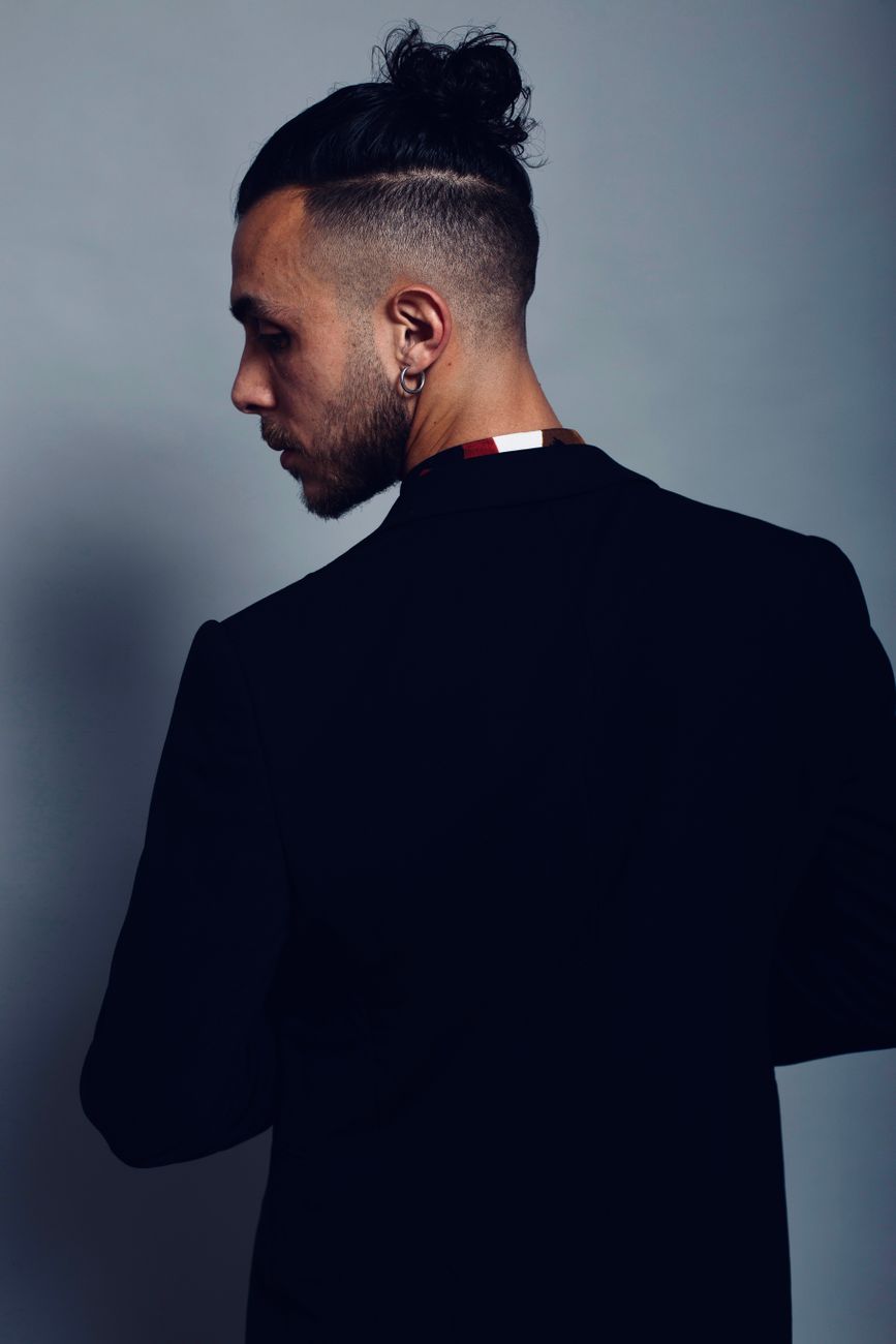 Homme de profil, chignon haut et côtés dégradés courts, veste sombre